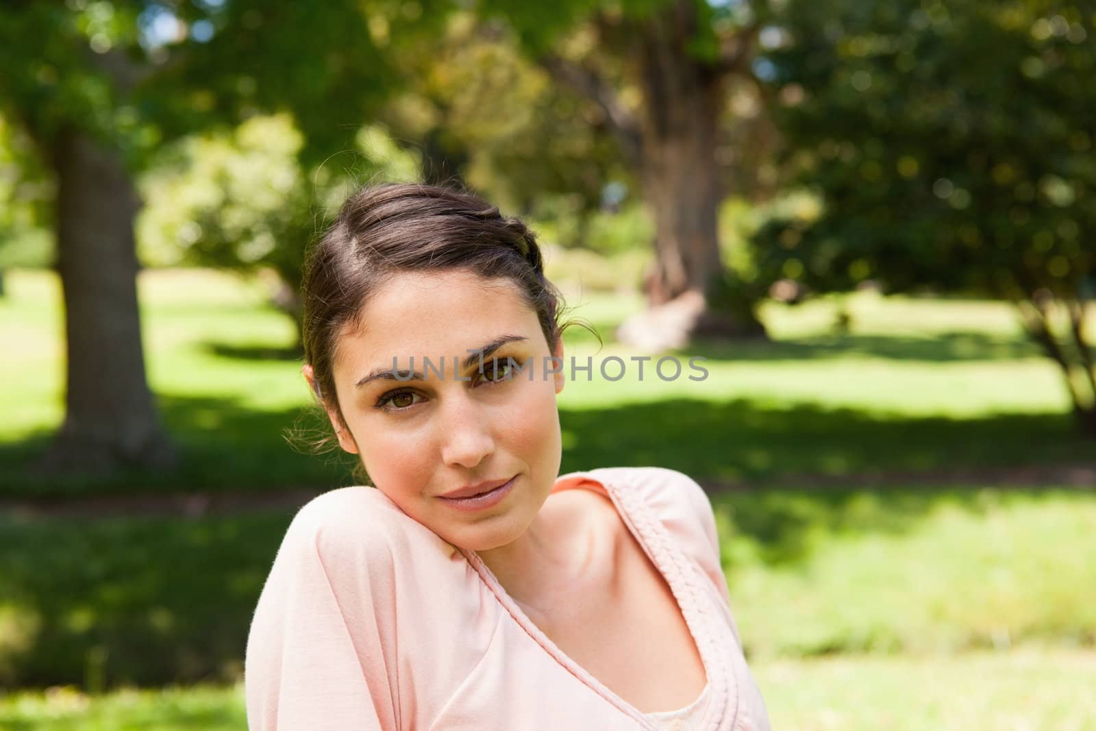 Woman with a serious expression on her face looking straight ahead with a view of trees in the backgroud