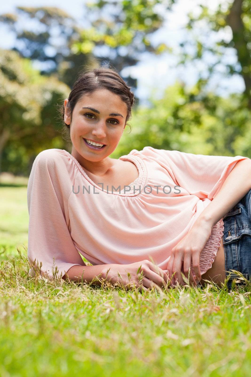 Woman smiling and looking straight ahead as she lies down on her side on the grass