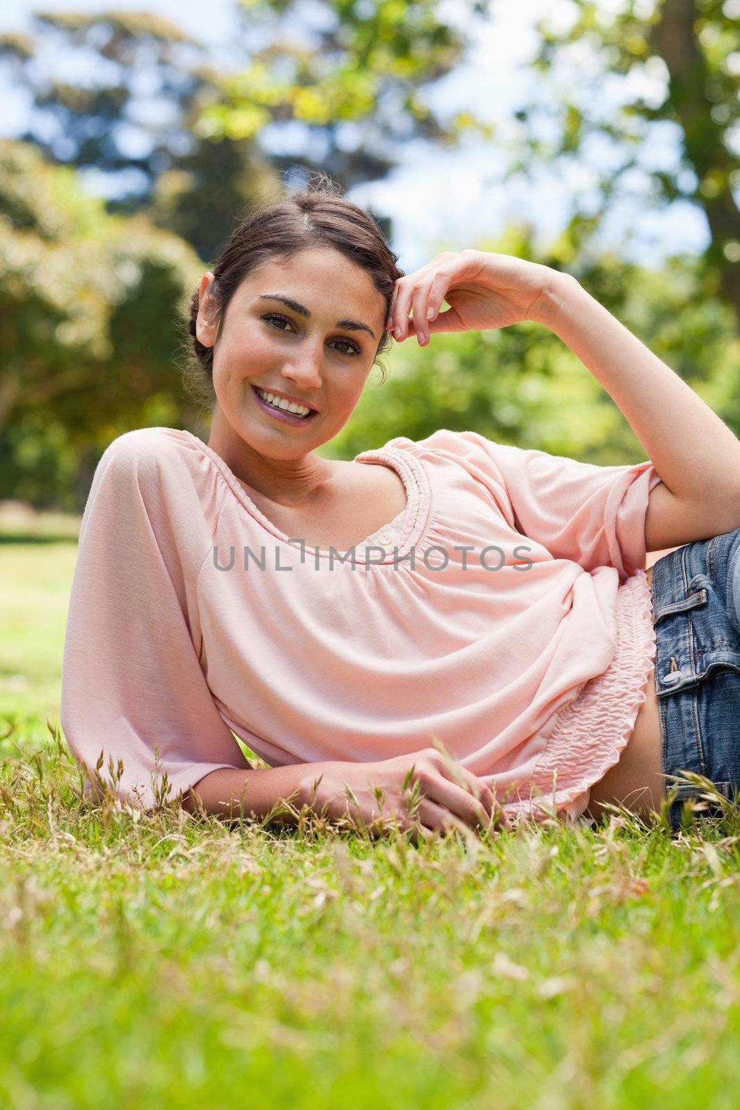 Smiling woman with her head tilted resting her head against her arm while lying down on grass