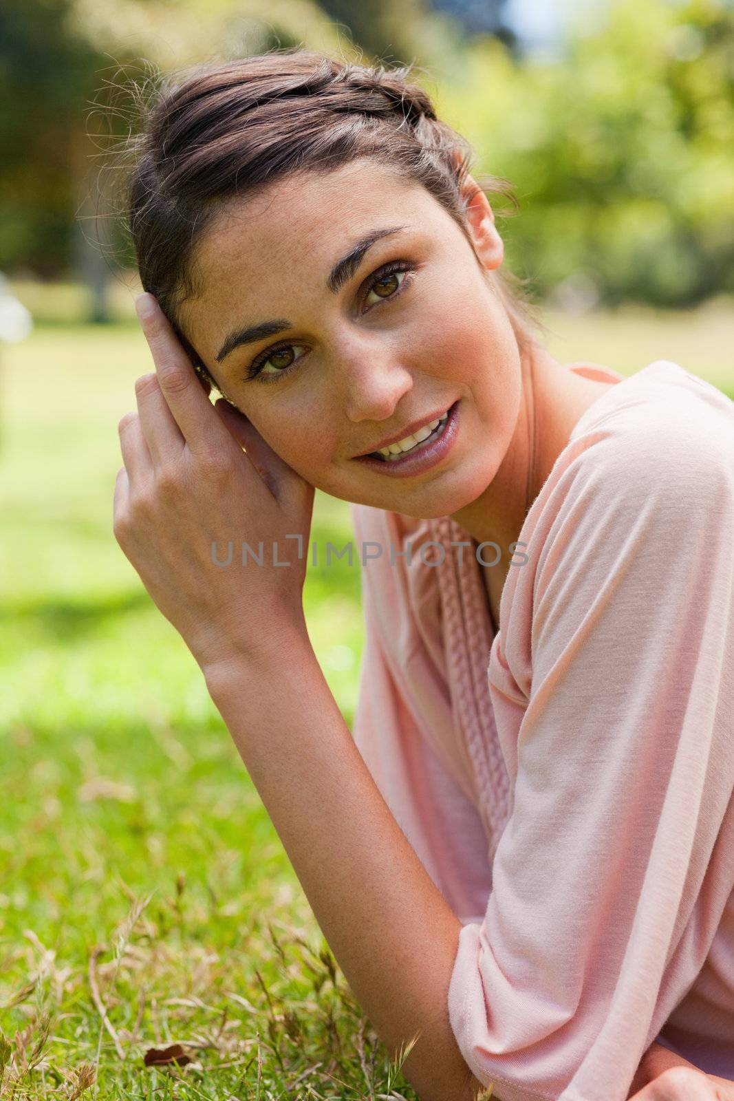 Smiling woman tilting her head against her hands while lying on her front on the grass