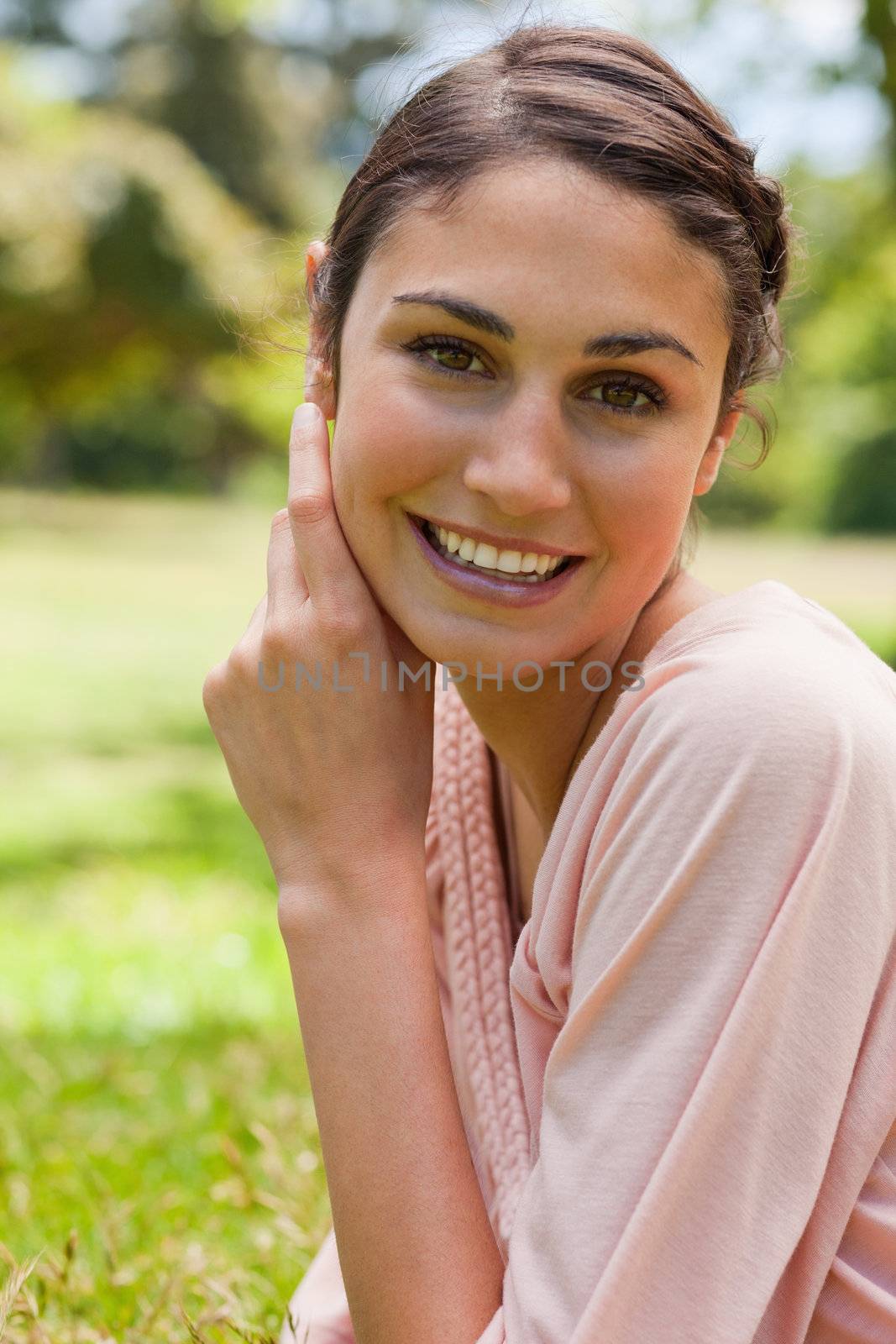 Smiling woman resting her head against her hands while lying on her front on the grass