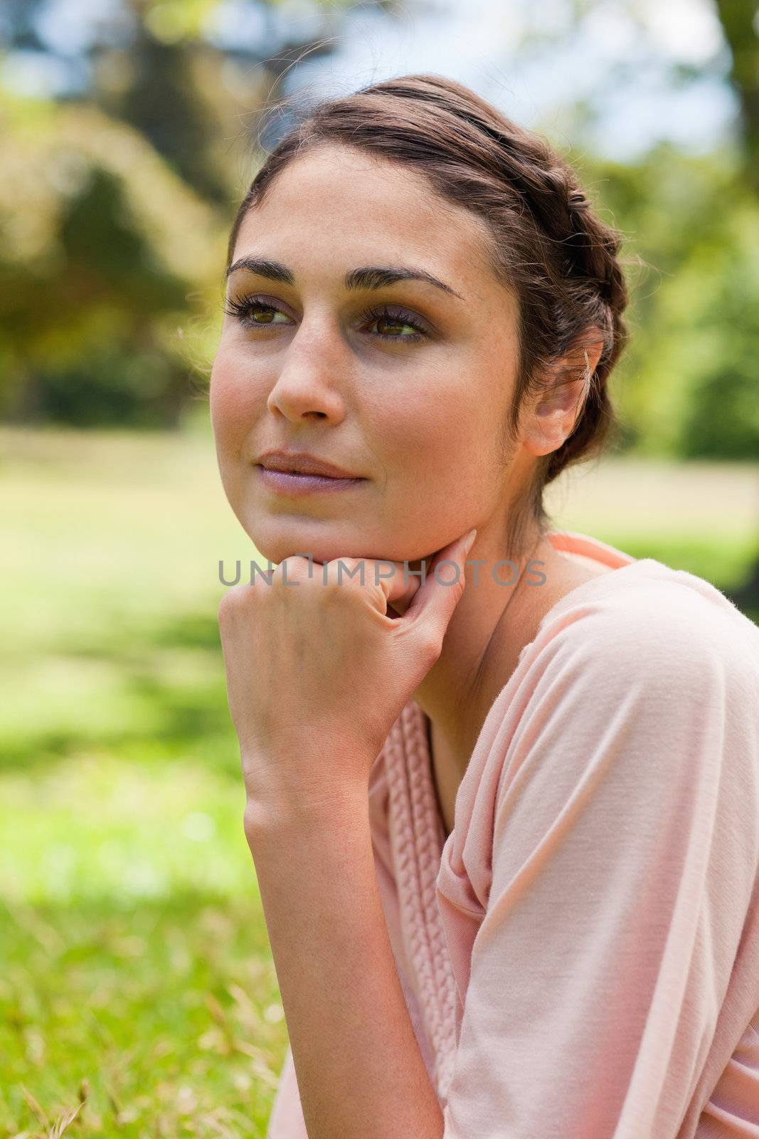 Woman looking straigh ahead of her while resting her head on her fist as she is sitting on the grass