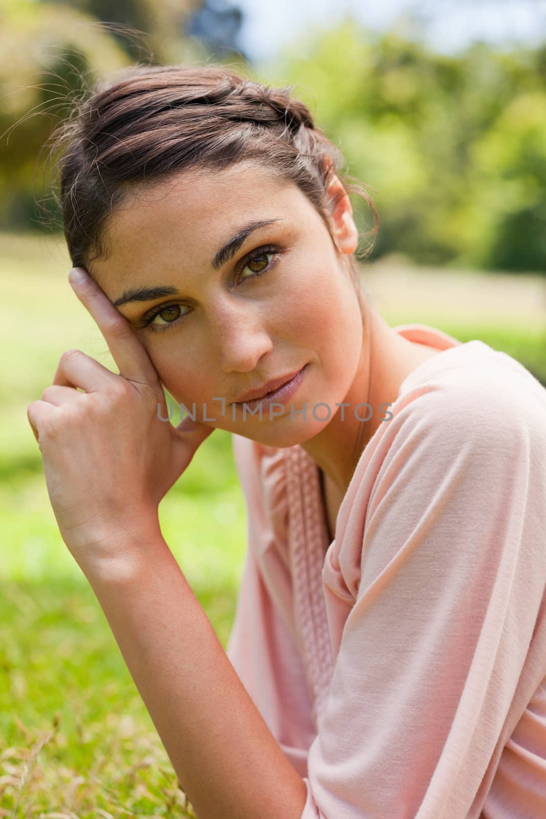 Woman with a serious expression tilting her head against her fingers as she lays on front in the grass