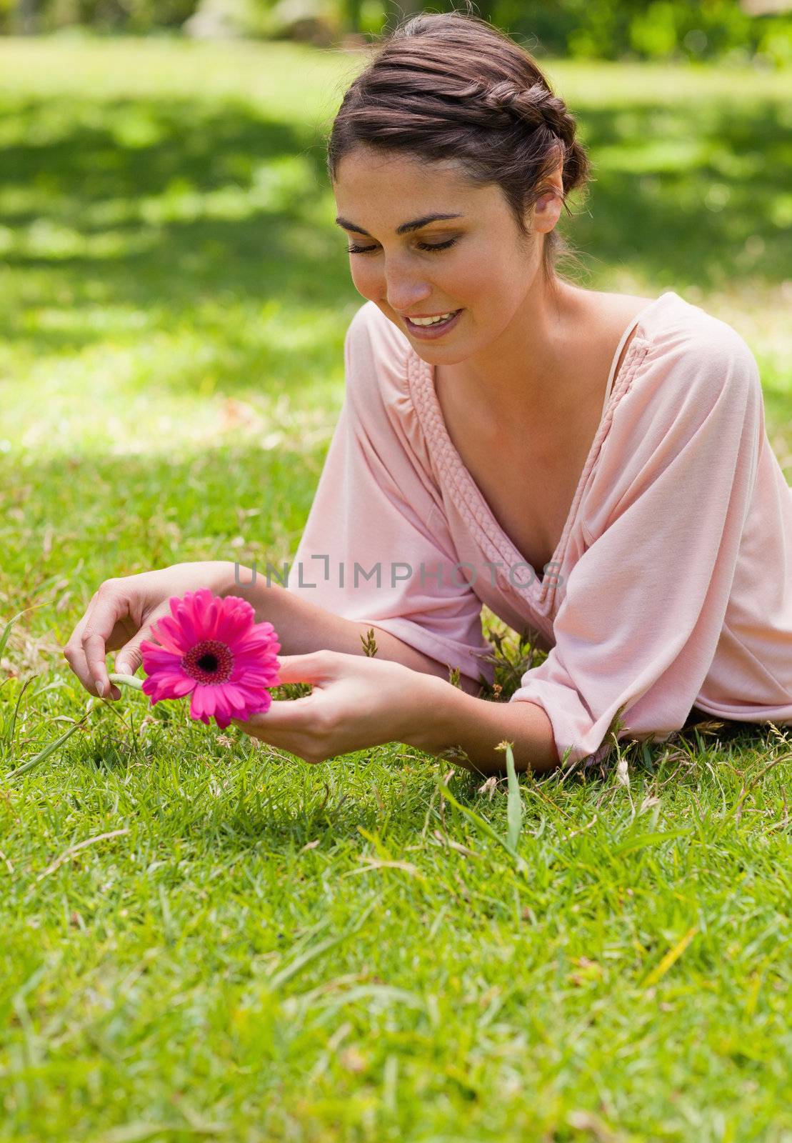 Smiling woman holding a pink flower while lying on her front in grass