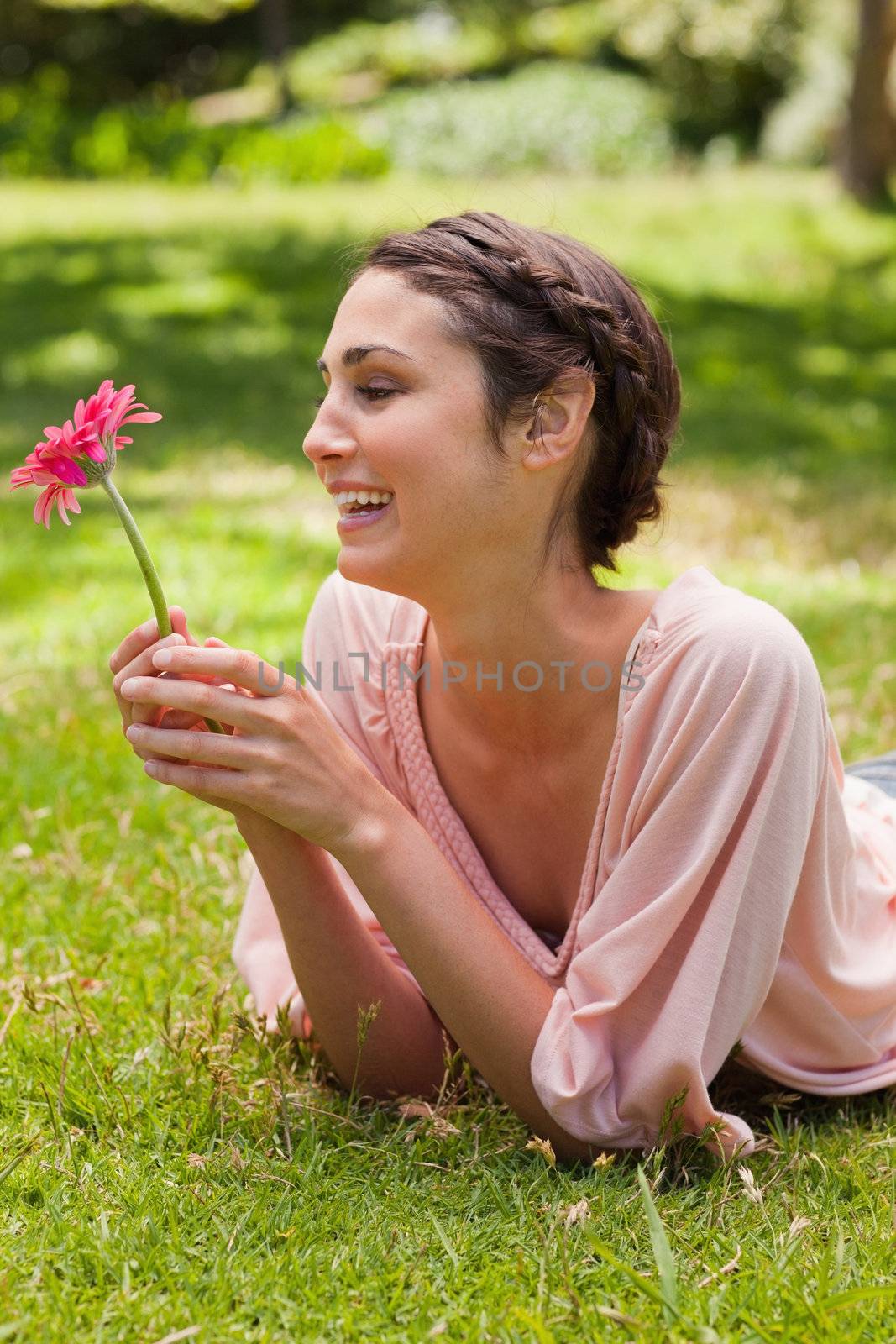 Young woman lying on her front laughing while looking at a flower which is being held in her hand
