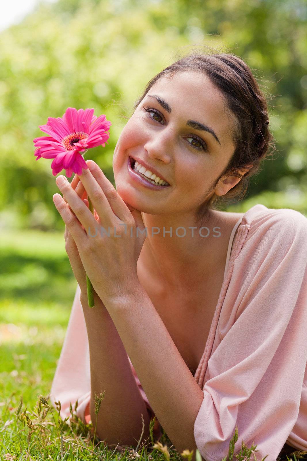 Smiling woman lying on her front and resting her chin on her arms while holding a pink flower