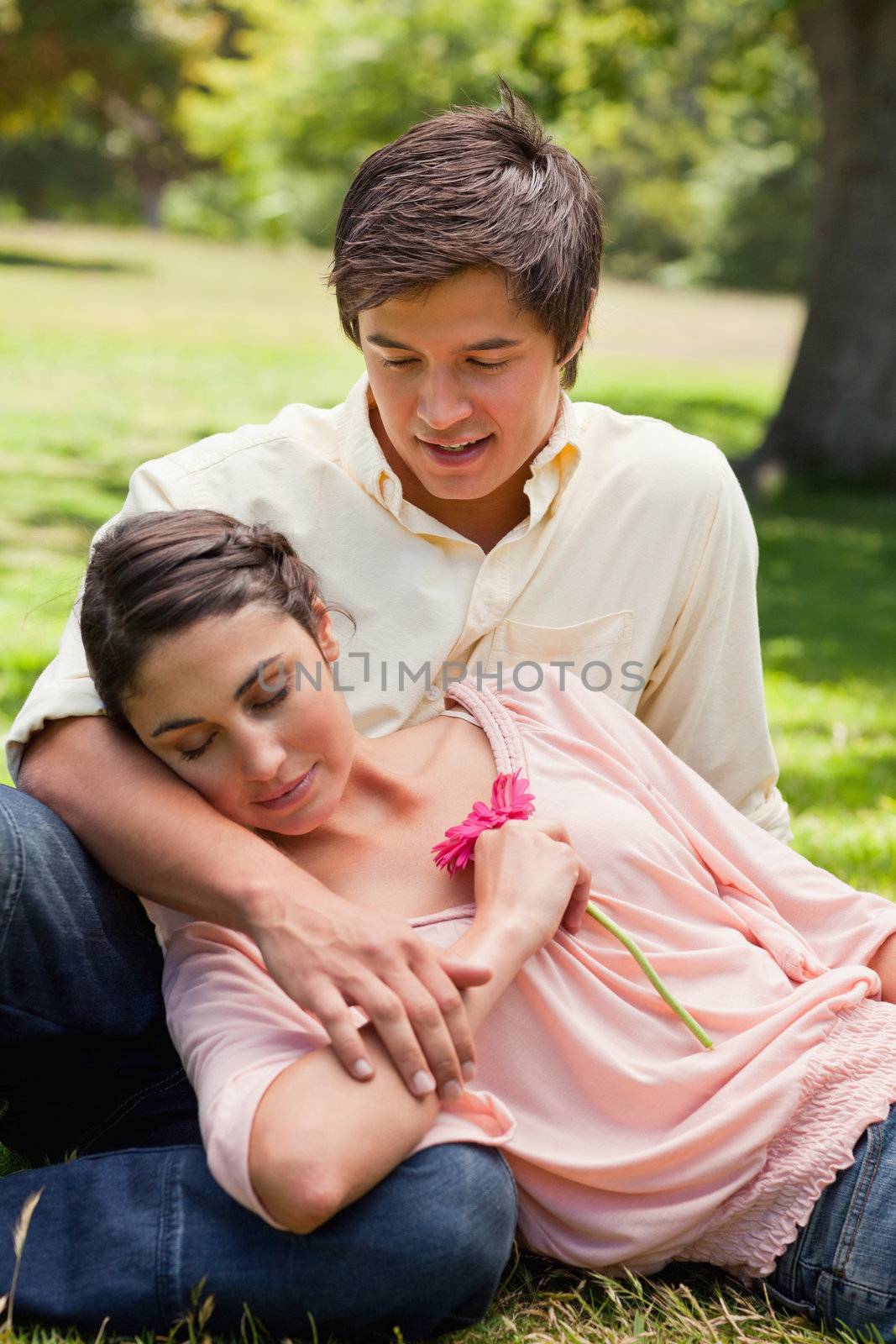 Man smiling as he looks at his friend who is lying against him as he is sitting down on the grass