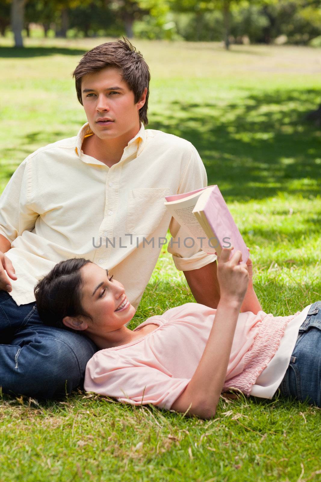 Woman lying against her friend's leg while she is reading by Wavebreakmedia