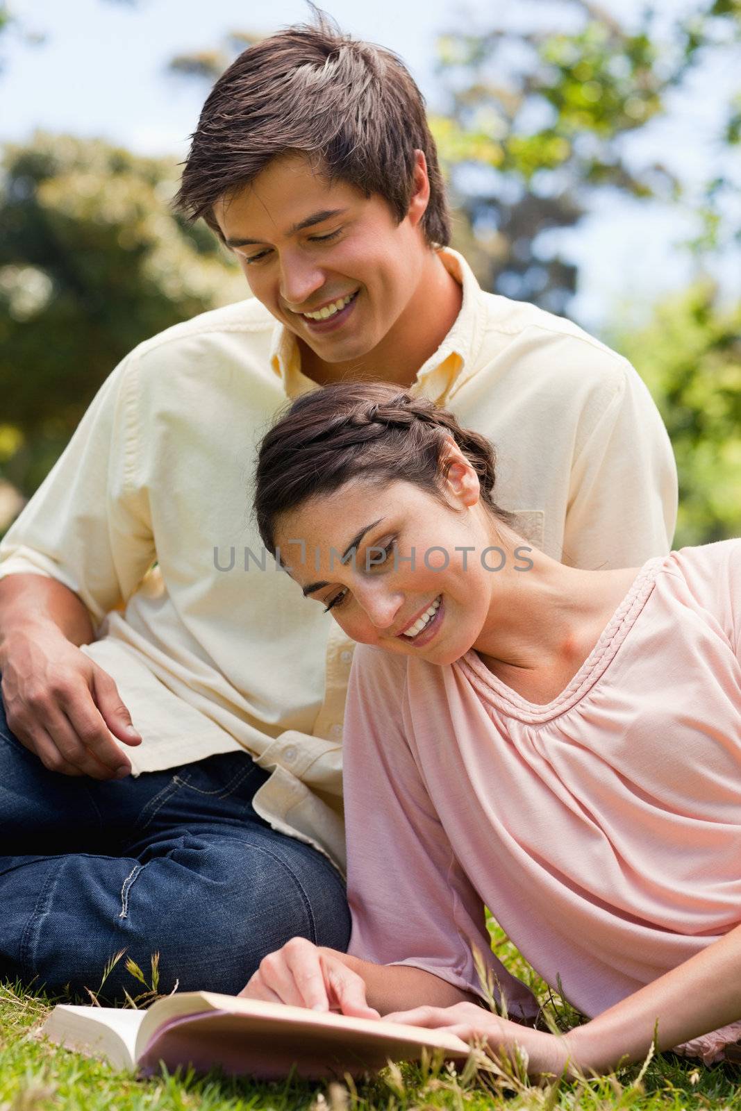 Two friends reading a book while lying down together by Wavebreakmedia