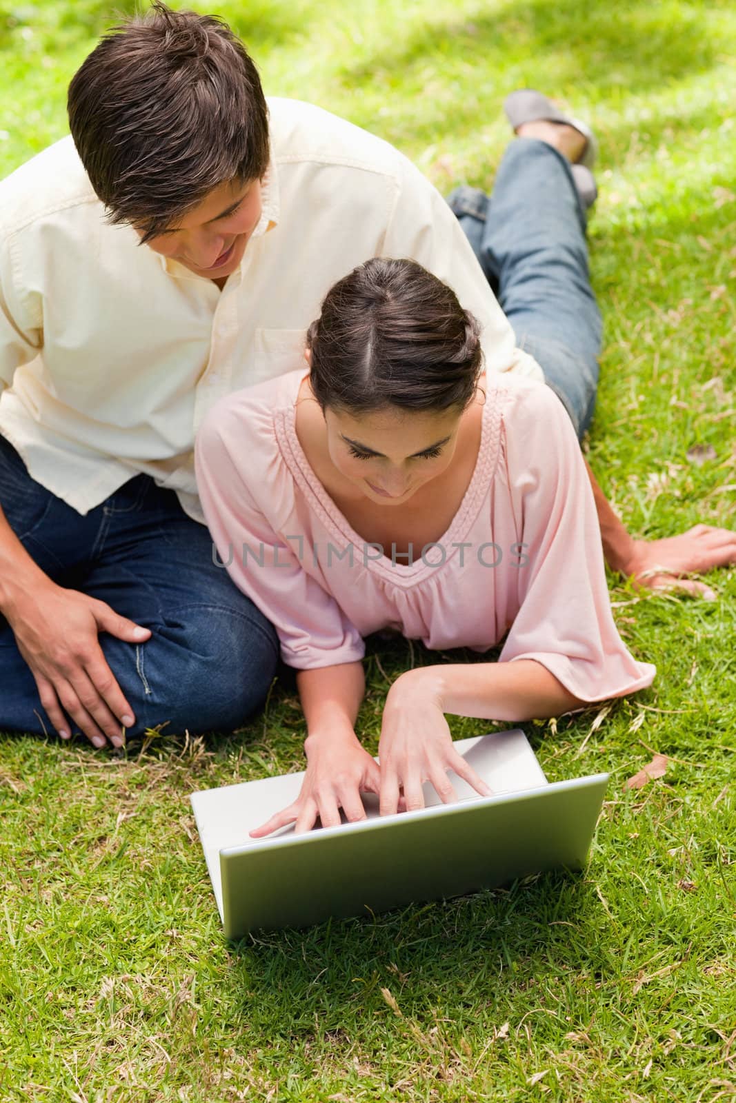 Two friends using a silver laptop together while lying down in the grass