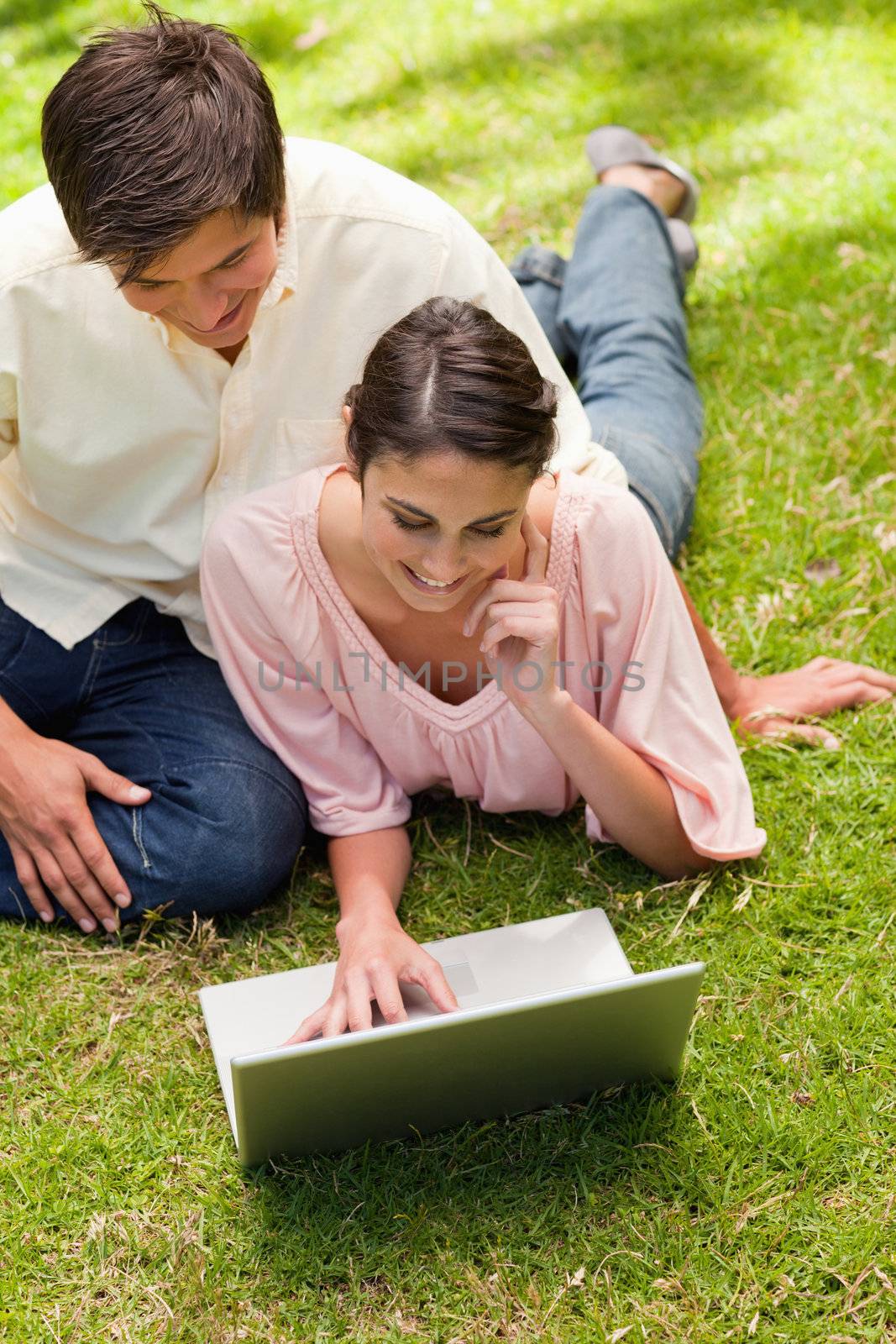 Woman resting her face against her hand while using a silver laptop with her friend sitting next to her on the grass