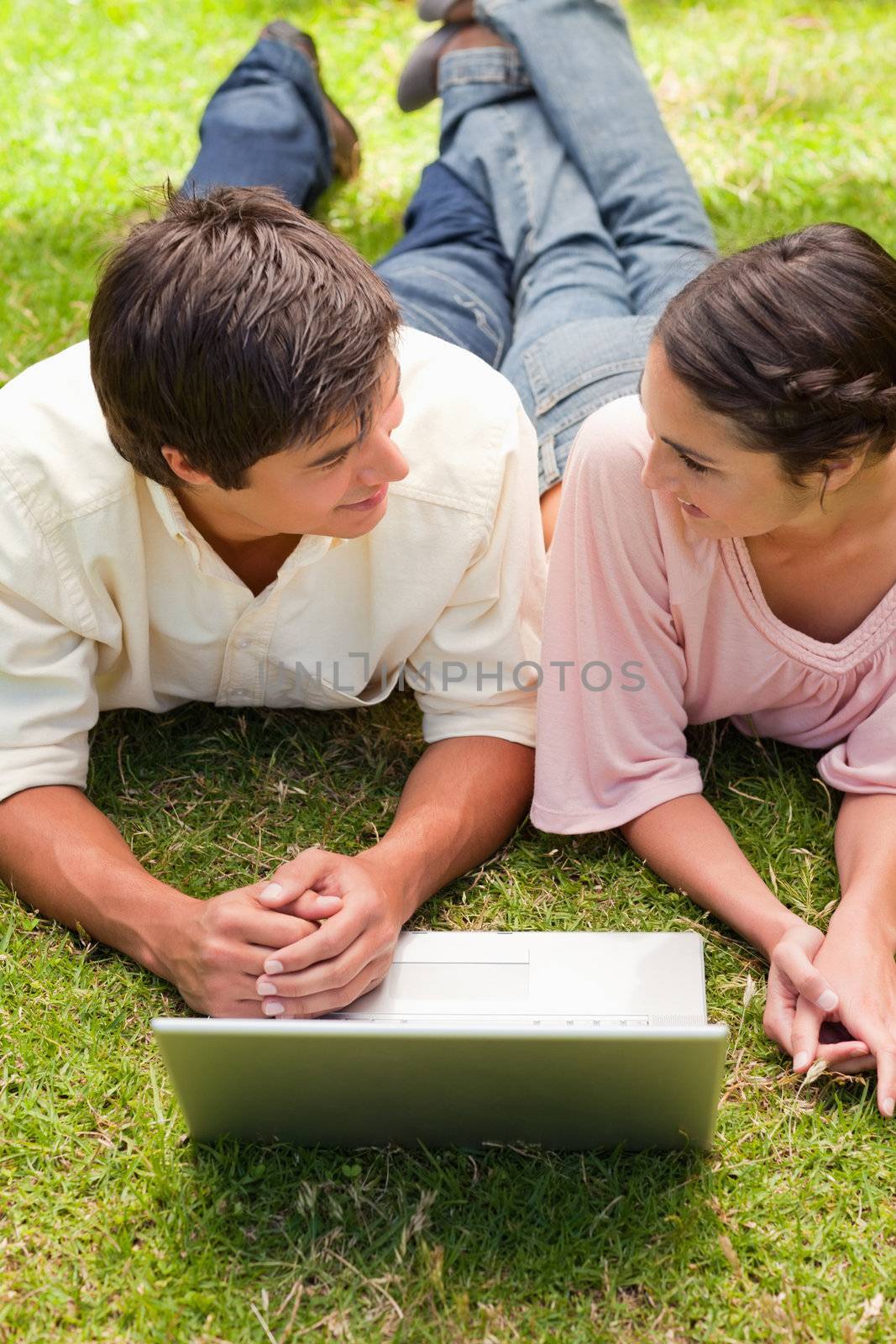 Two friends looking at each other as they lie down with a laptop by Wavebreakmedia