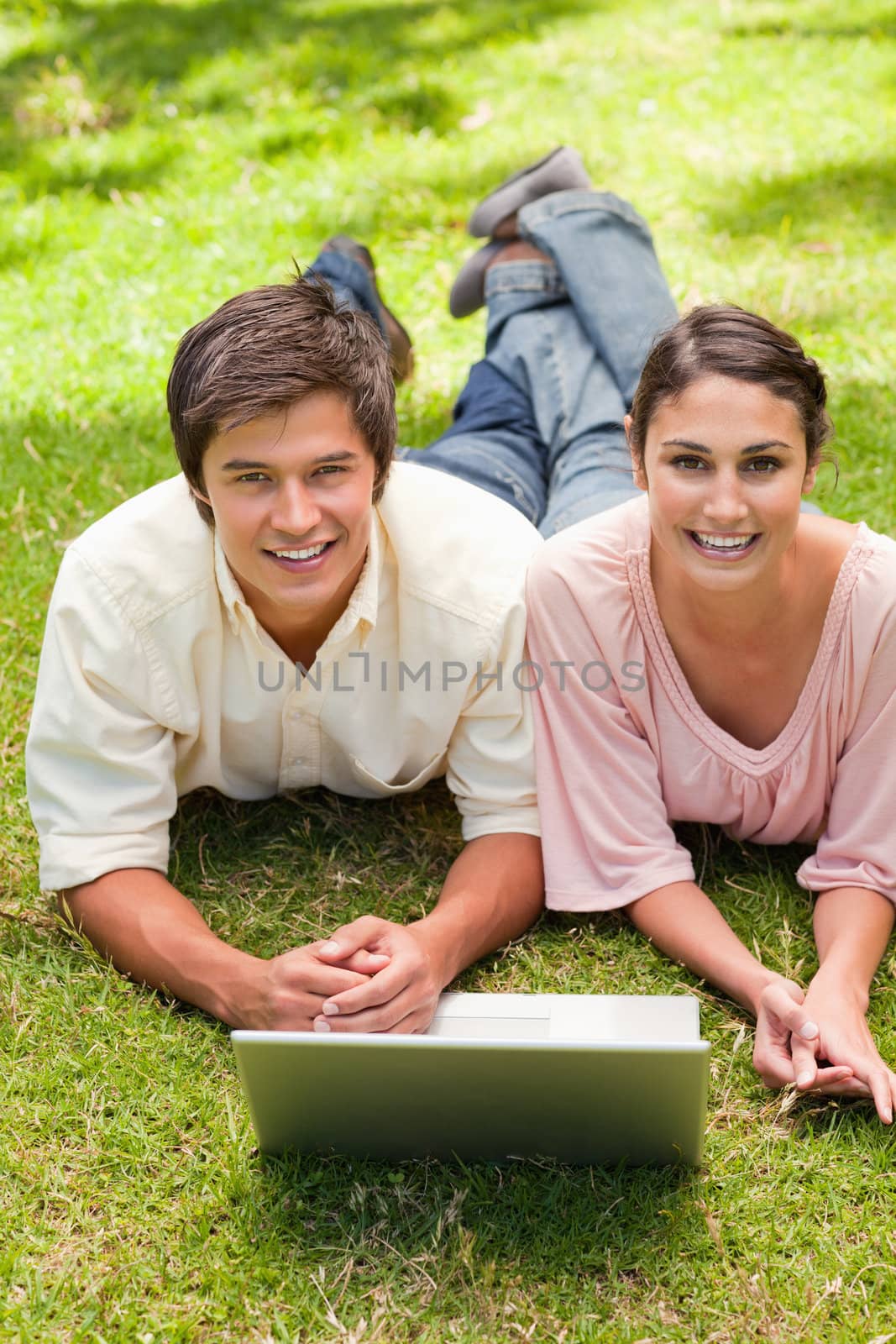 Two friends laughing while looking ahead as they use a laptop by Wavebreakmedia