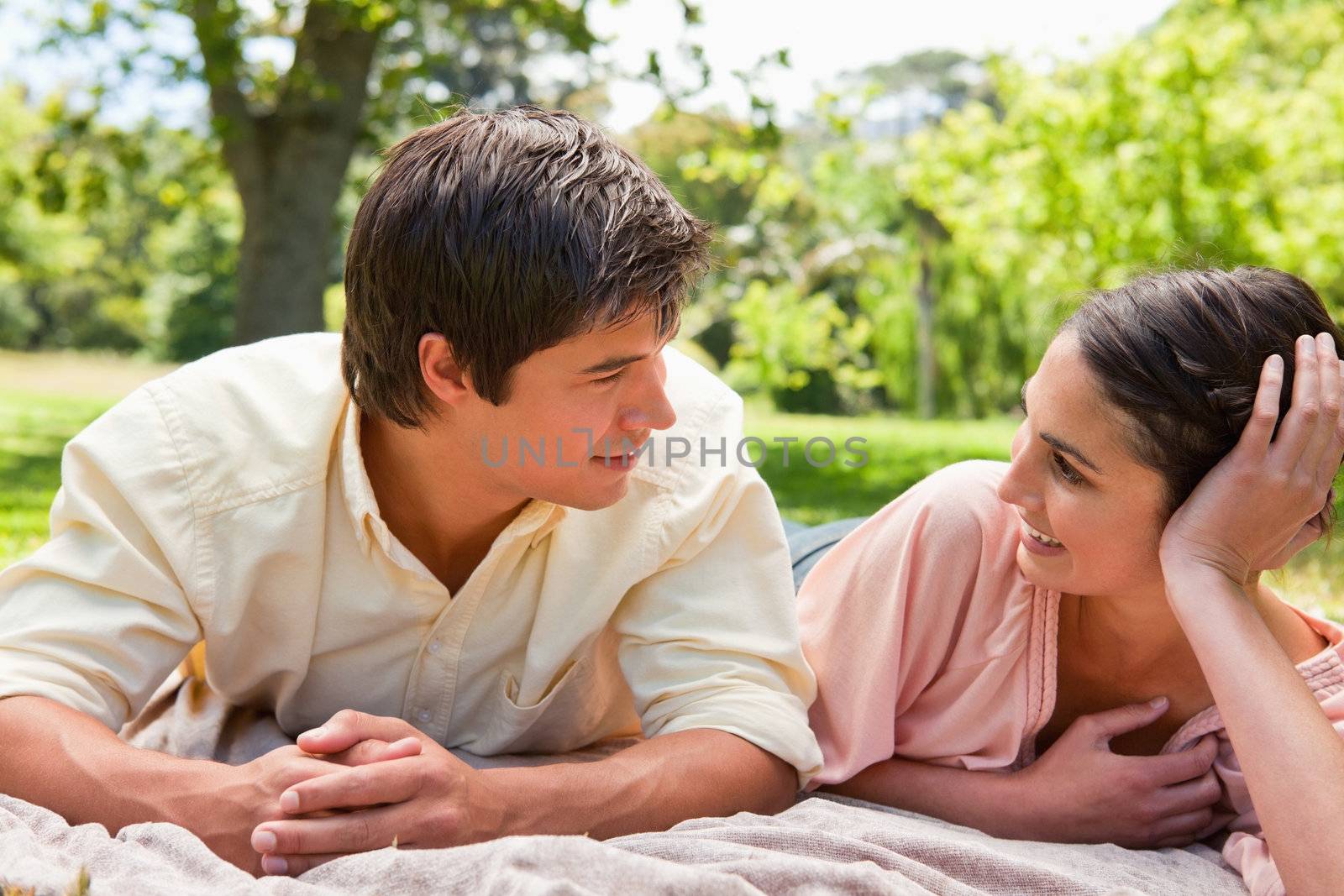 Man and a woman smiling while looking at each other as they lie on a grey blanket