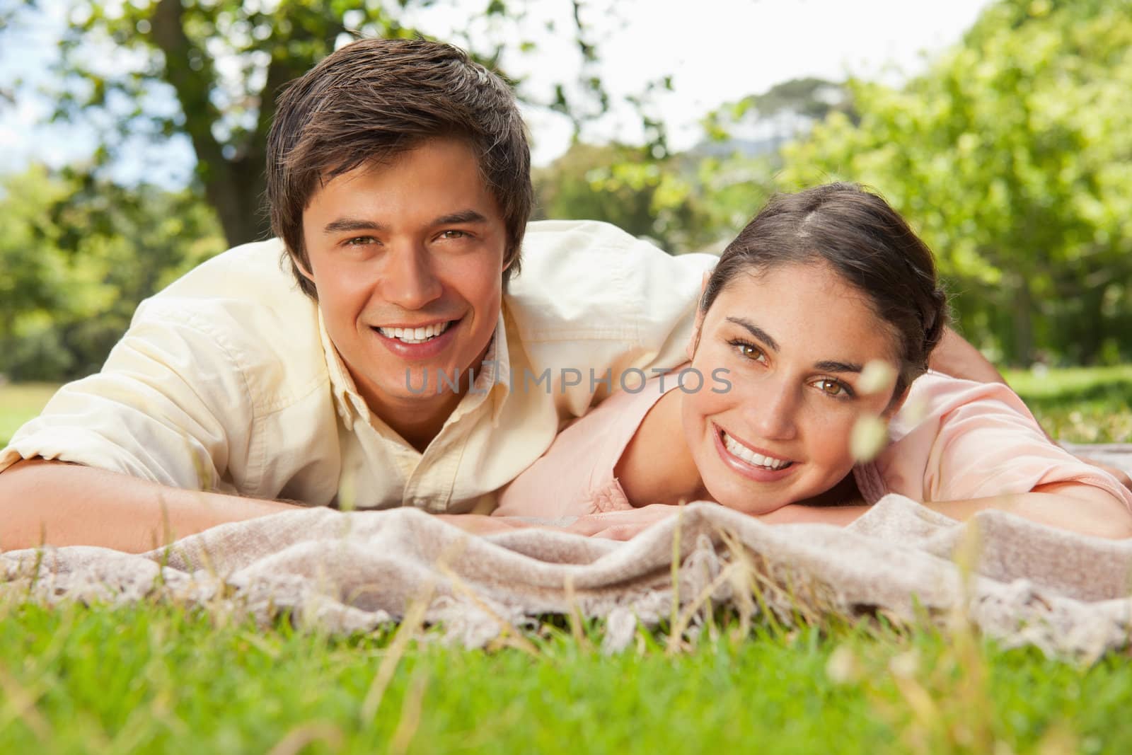 Two friends smiling and looking ahead while lying on a blanket by Wavebreakmedia