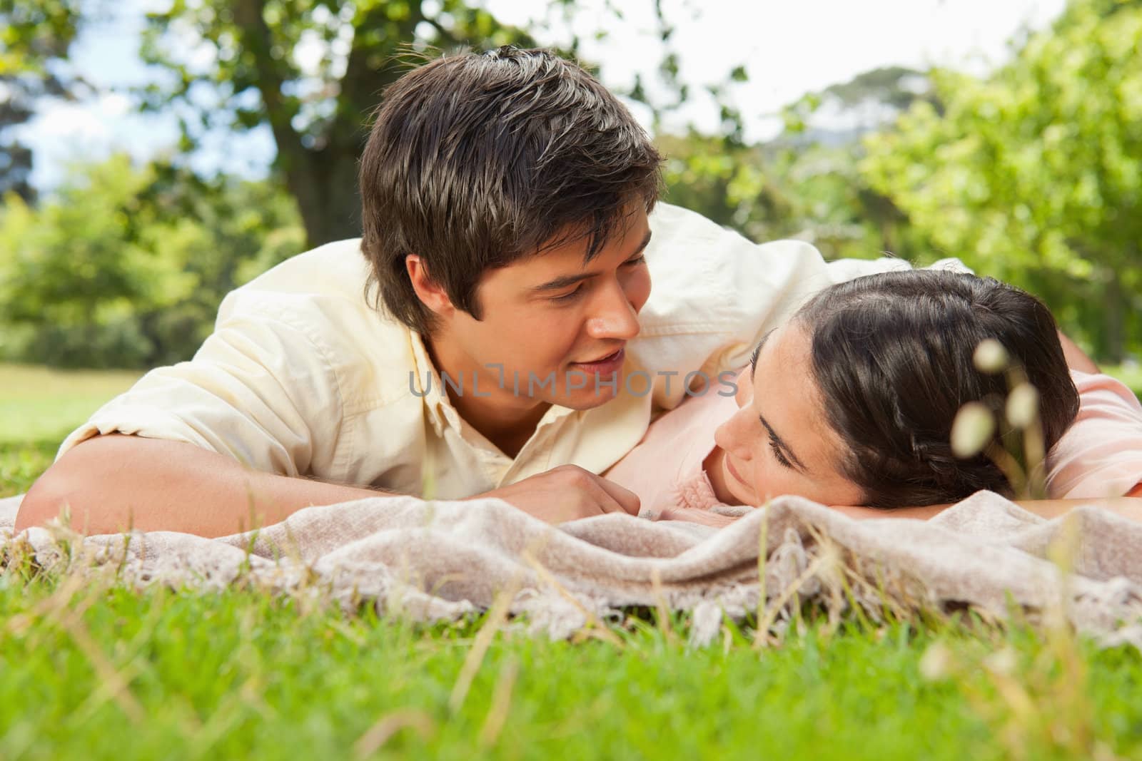 Man and a woman looking into each others eyes while lying prone on a grey blanket in the grass