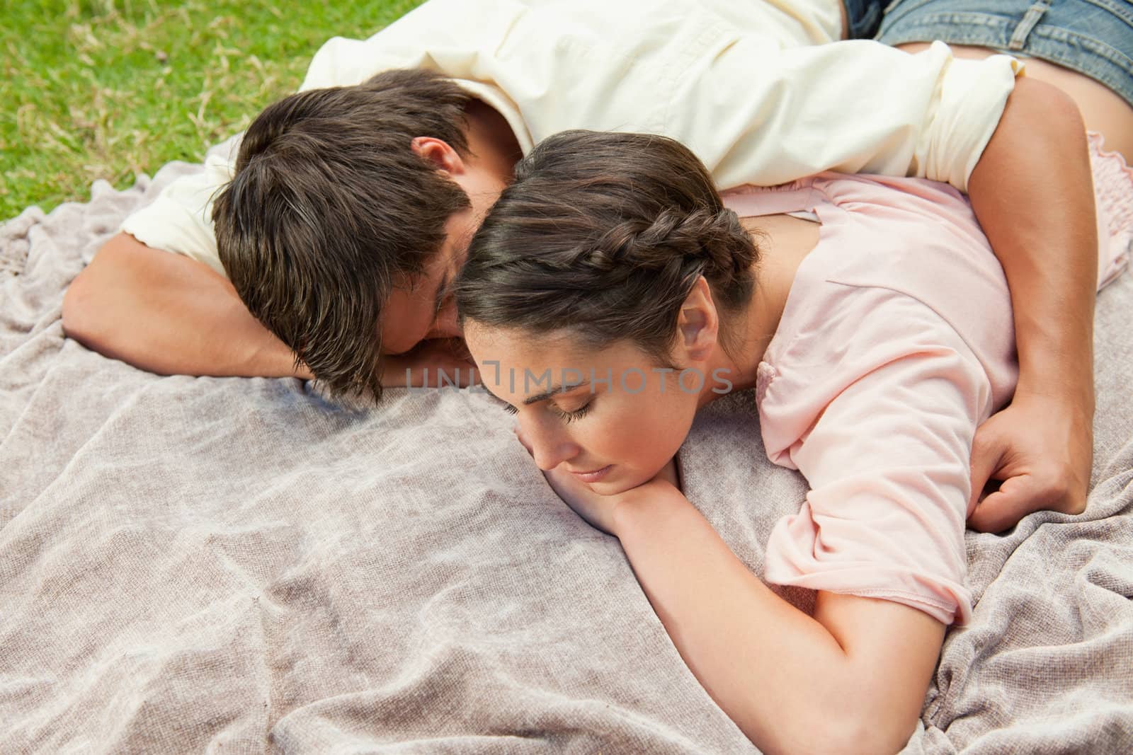 Man with his arm around his female friend while they are lying prone on a grey blanket int the grass