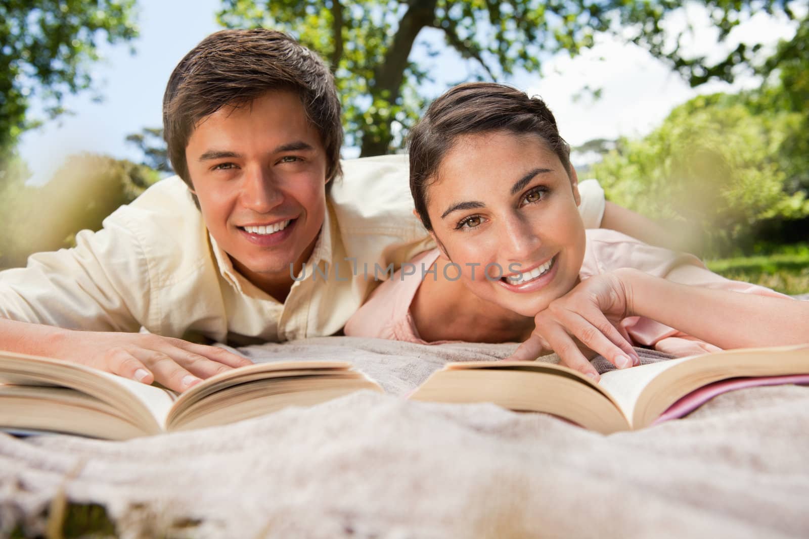Man and woman reading books together while lying prone on a grey blanket in the grass
