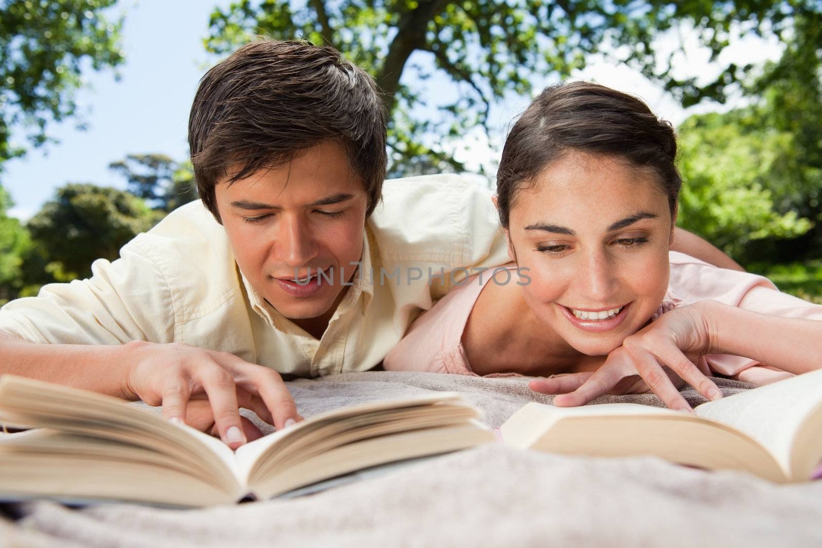 Two friends smiling while reading books as they lie down by Wavebreakmedia