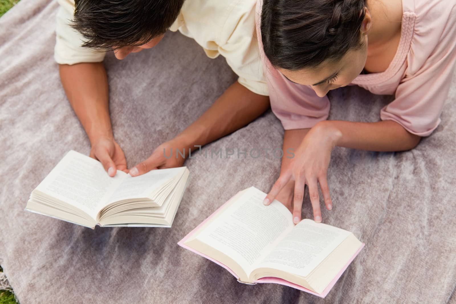 Elevated view of a man and a woman reading books while lying prone on a blanket in the grass