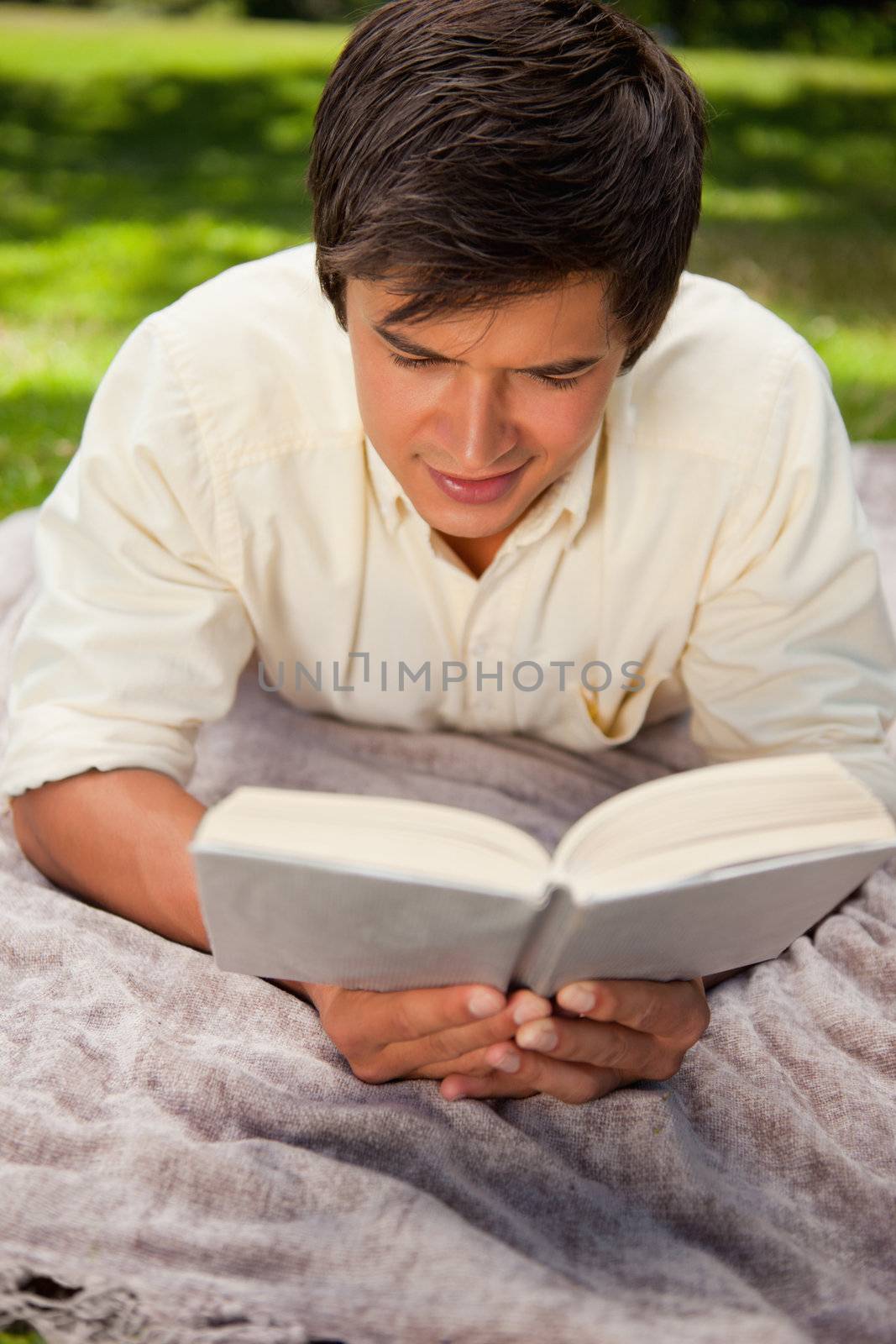 Man reads a books as he lies on a grey blanket in the grass 