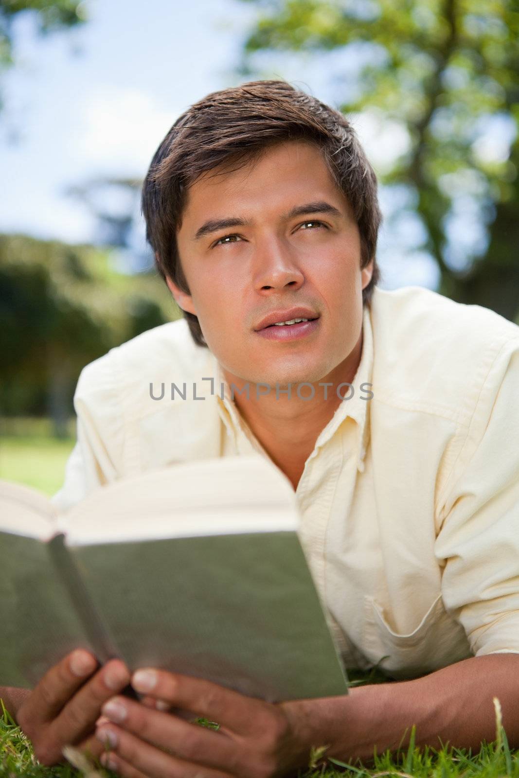 Man looks to the distance while reading a book as he is lying do by Wavebreakmedia