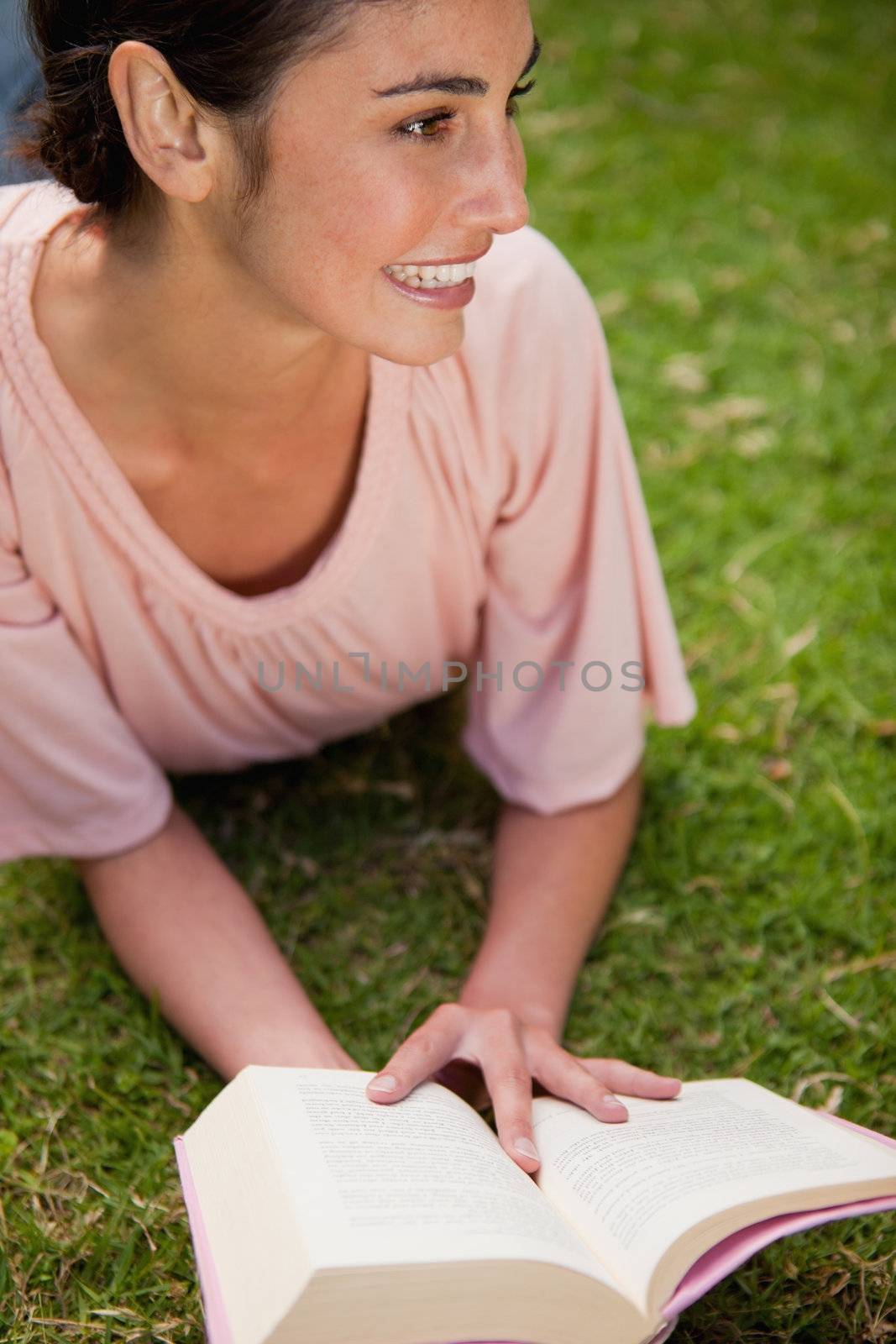 Woman looking towards the side while reading a book as she is lying down in grass