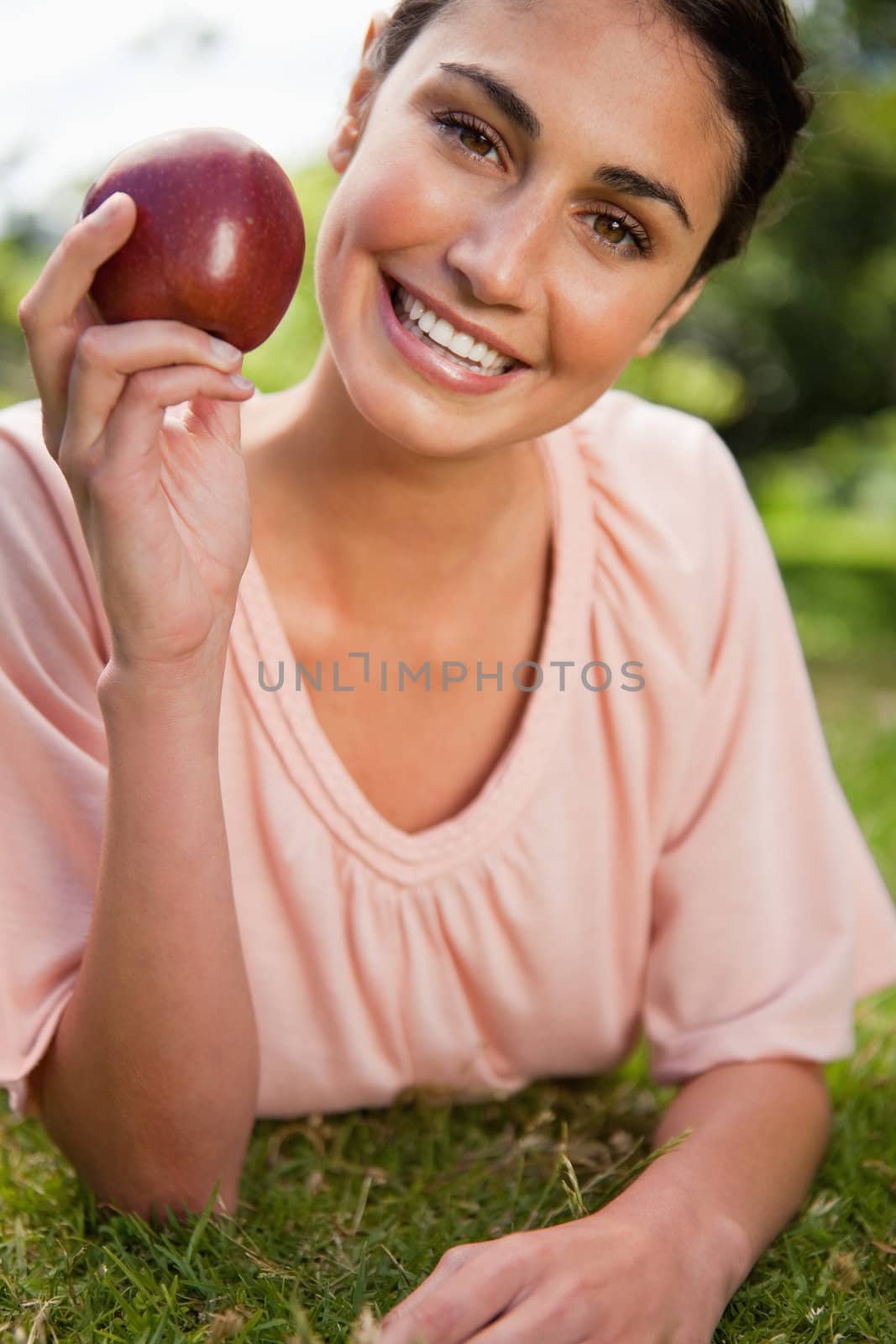 Woman smiles while holding a red apple as she is lying prone in grass