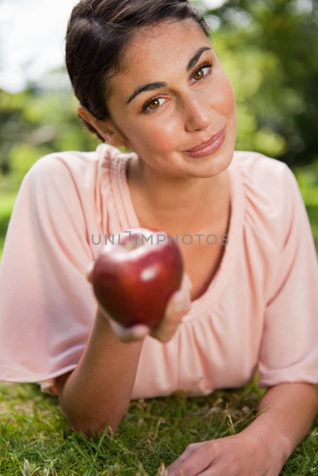 Woman offering a red apple while lying prone in the grass