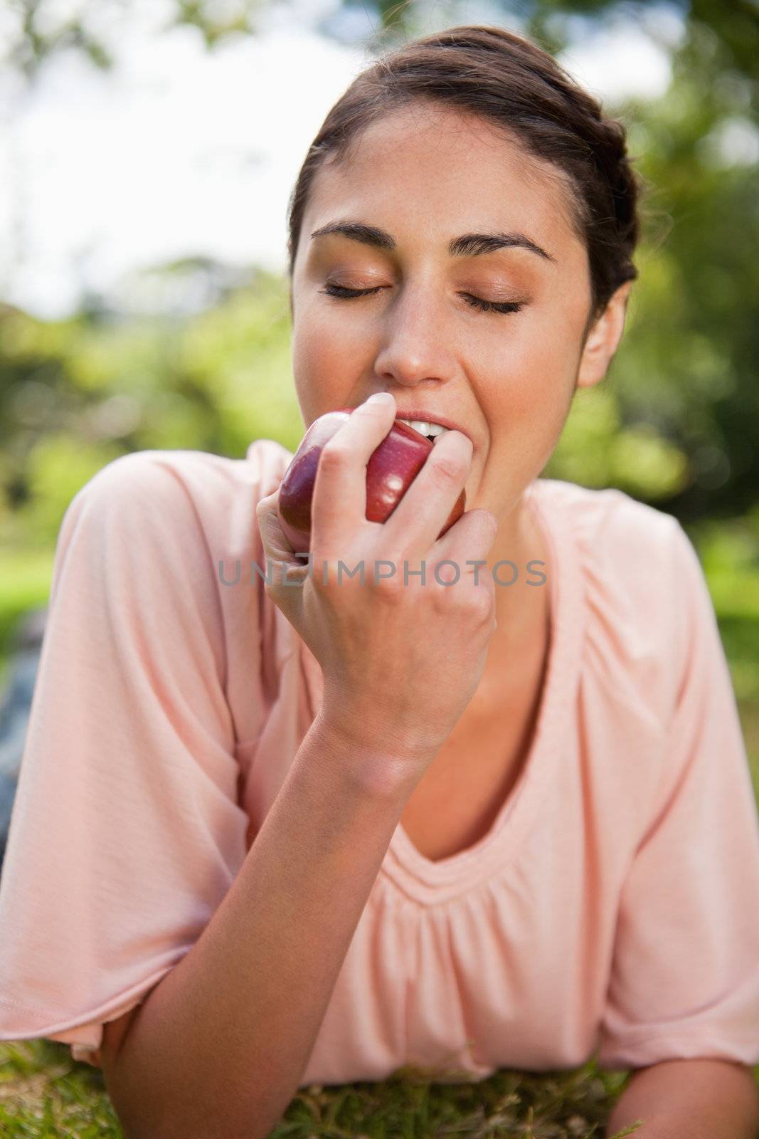Young woman bites into a red apple while lying prone in grass