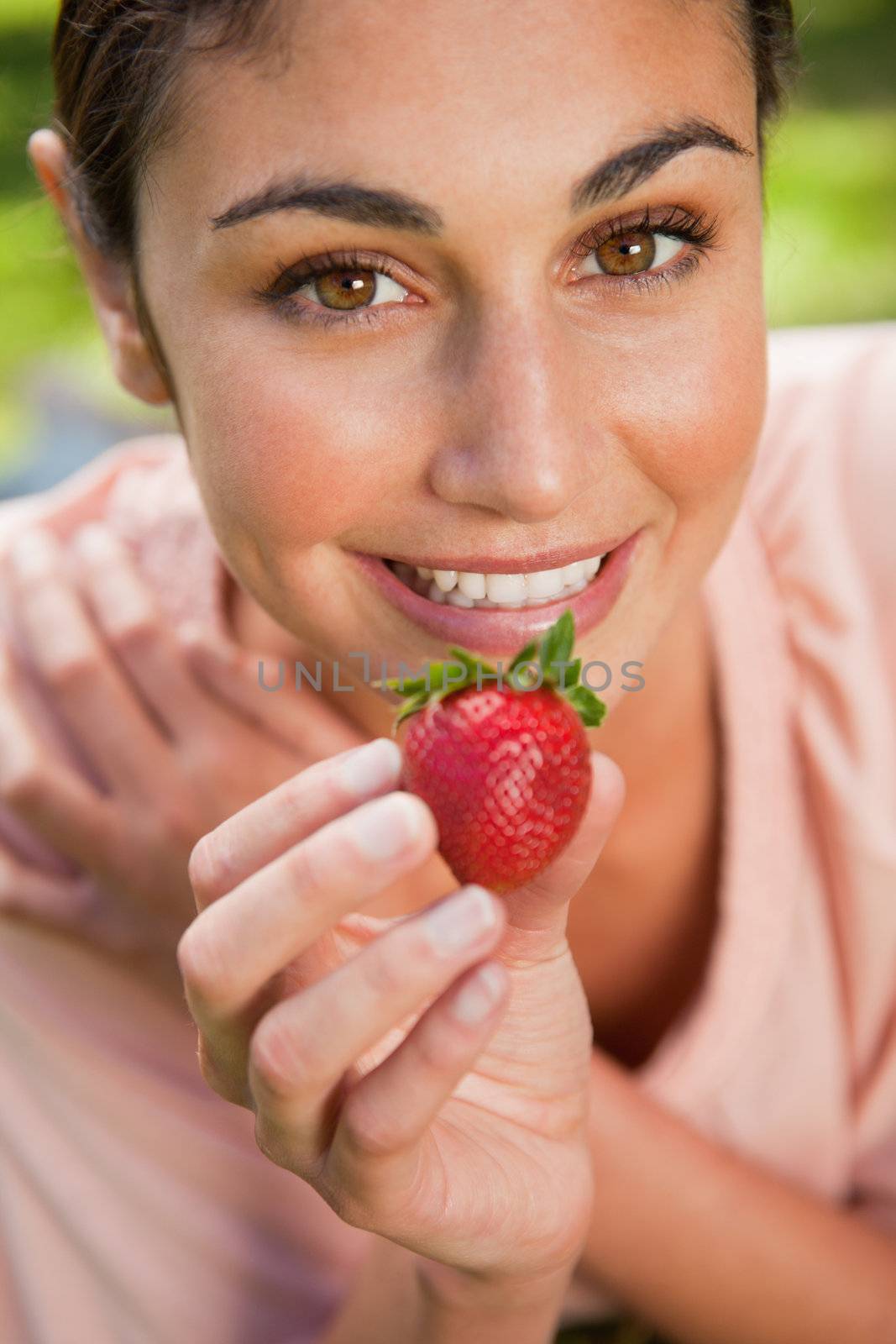 Woman smiling while offering a strawberry as she lies prone in grass