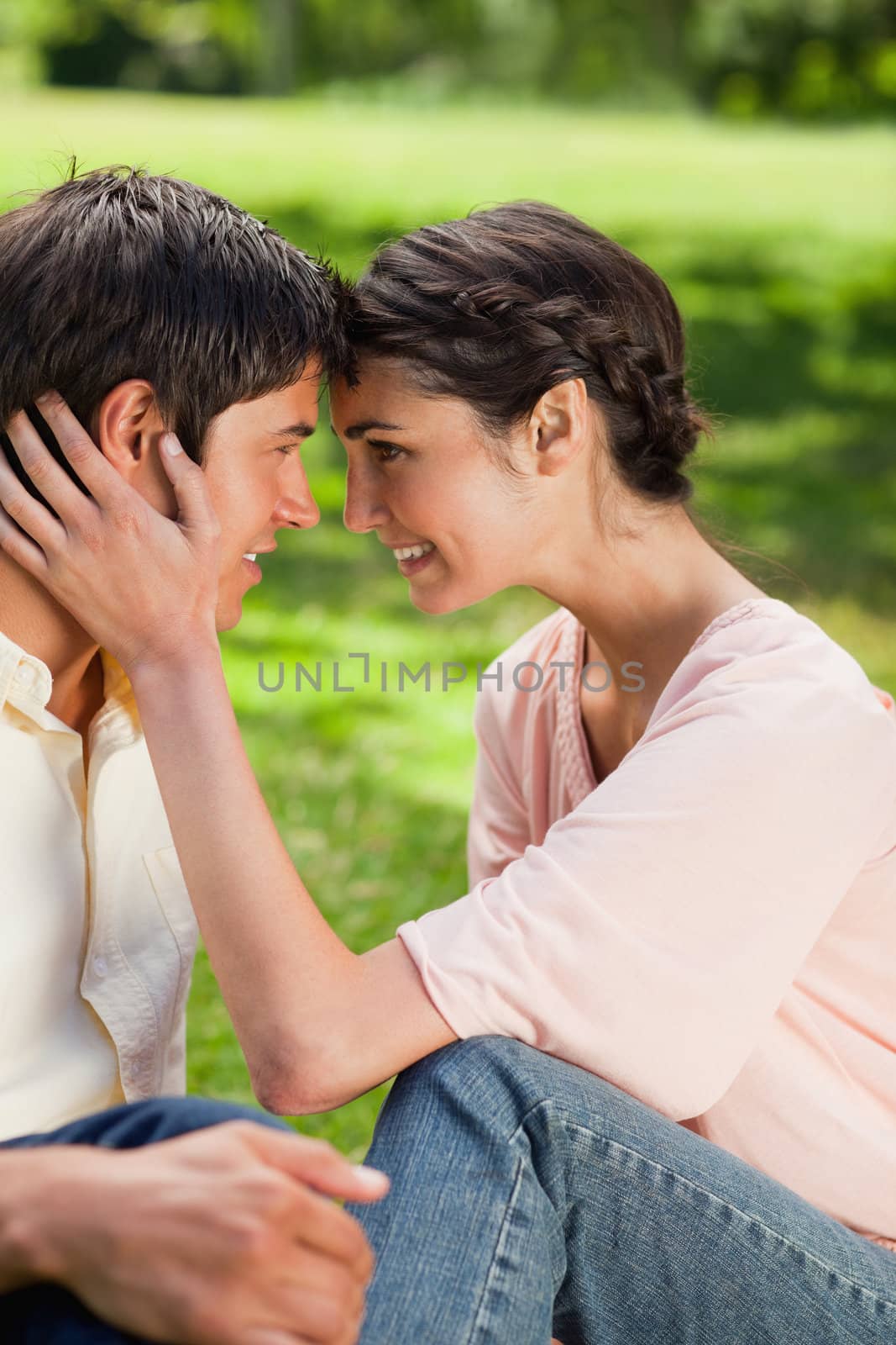 Woman smiling as she looks at her friend while they touch their heads together in a park