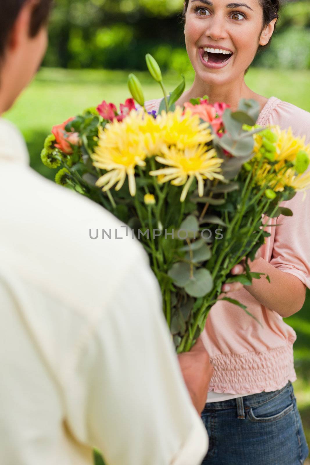 Woman surprised as she is presented with flowers by her friend by Wavebreakmedia