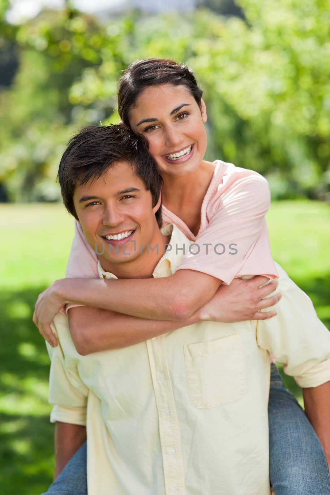 Woman smiling while looking in front of her as she is being carried bey her friend in a park