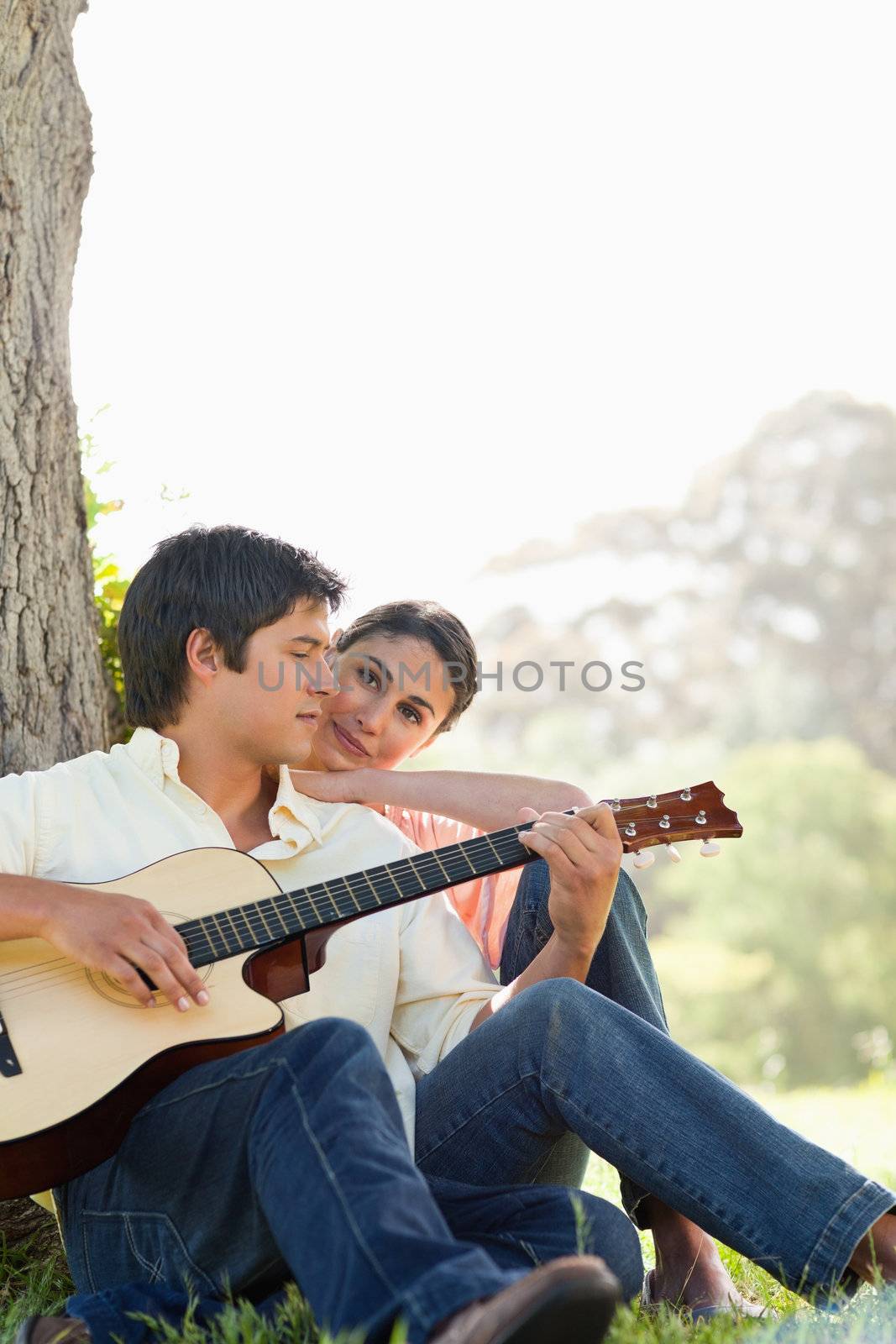 Man looking down while playing the guitar as his friend watches  by Wavebreakmedia