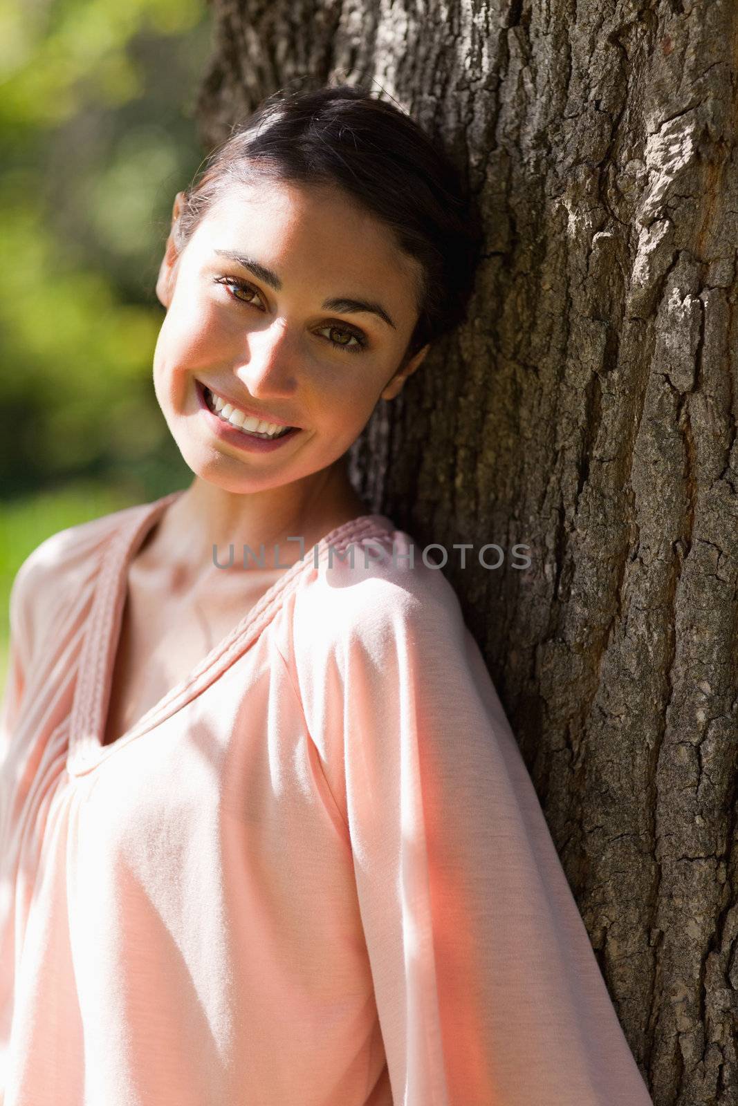 Woman looking towards the side while smiling as she sits against the trunk of a tree
