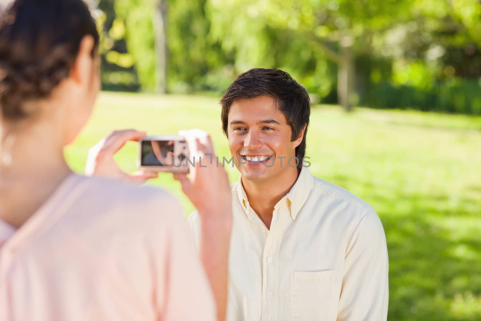 Using a camera, the woman takes a photo of her friend smiling in the park