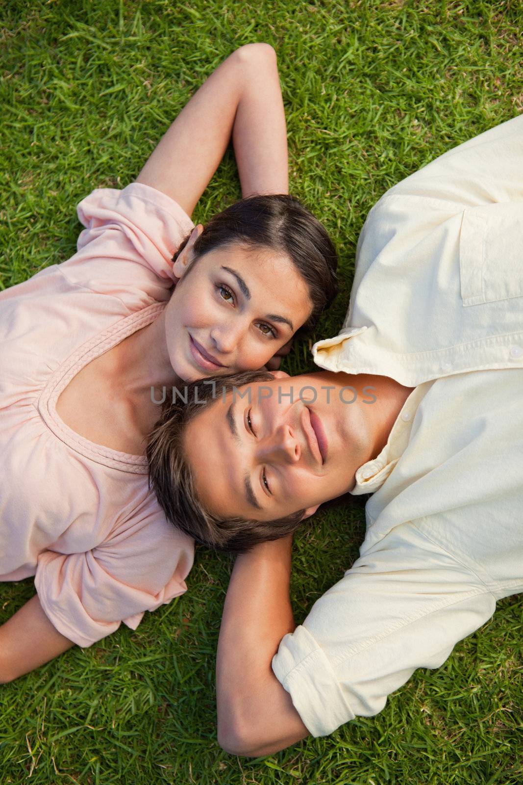 Woman with their eyes open lying head to shoulder with her arm resting behind her neck on the grass