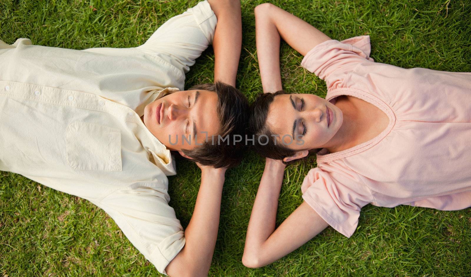 Two friends lying head to head with both hands behind their neck by Wavebreakmedia