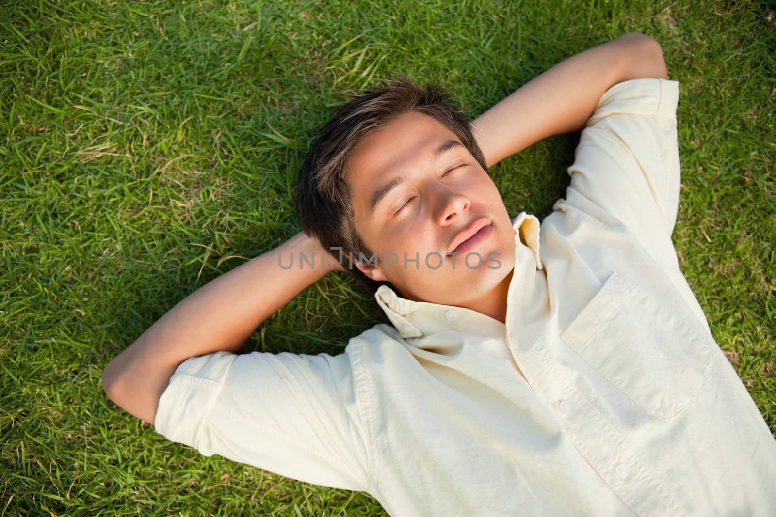 Man lying on the grass with his eyes closed and both hands resting behind his neck