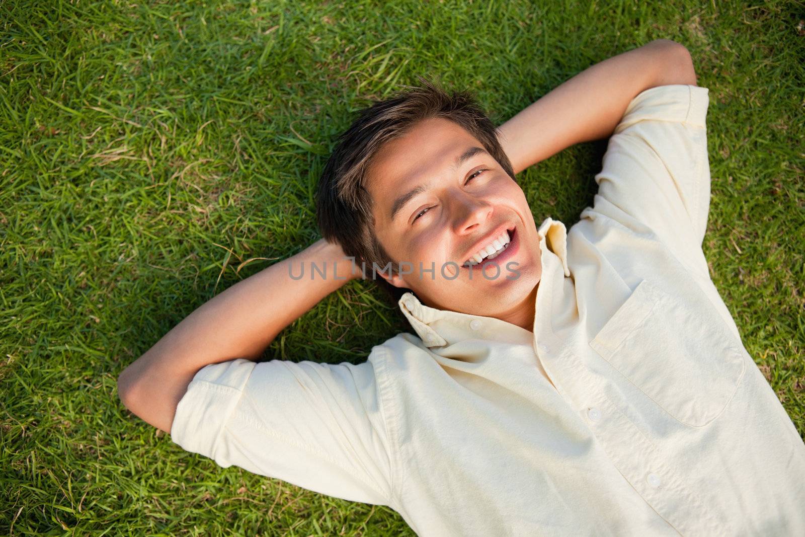 Smiling man lying with both hands resting behind his neck on the grass