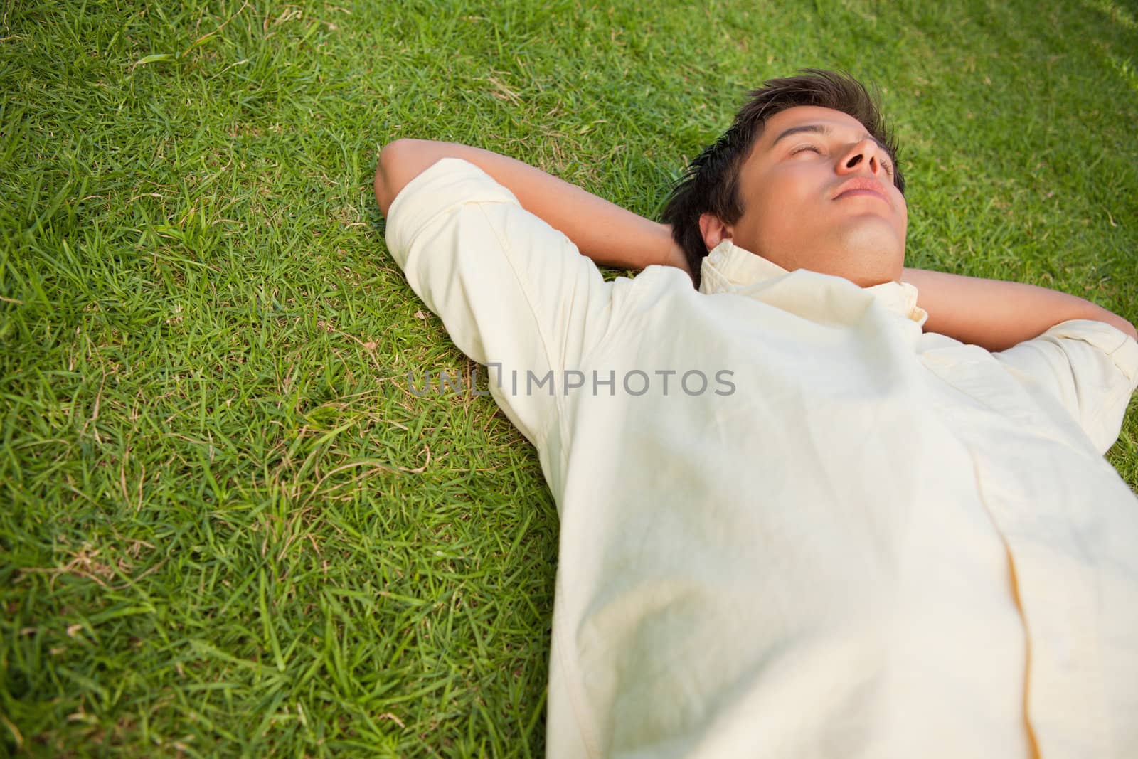 Man lying in grass with his eyes closed and his head resting on  by Wavebreakmedia