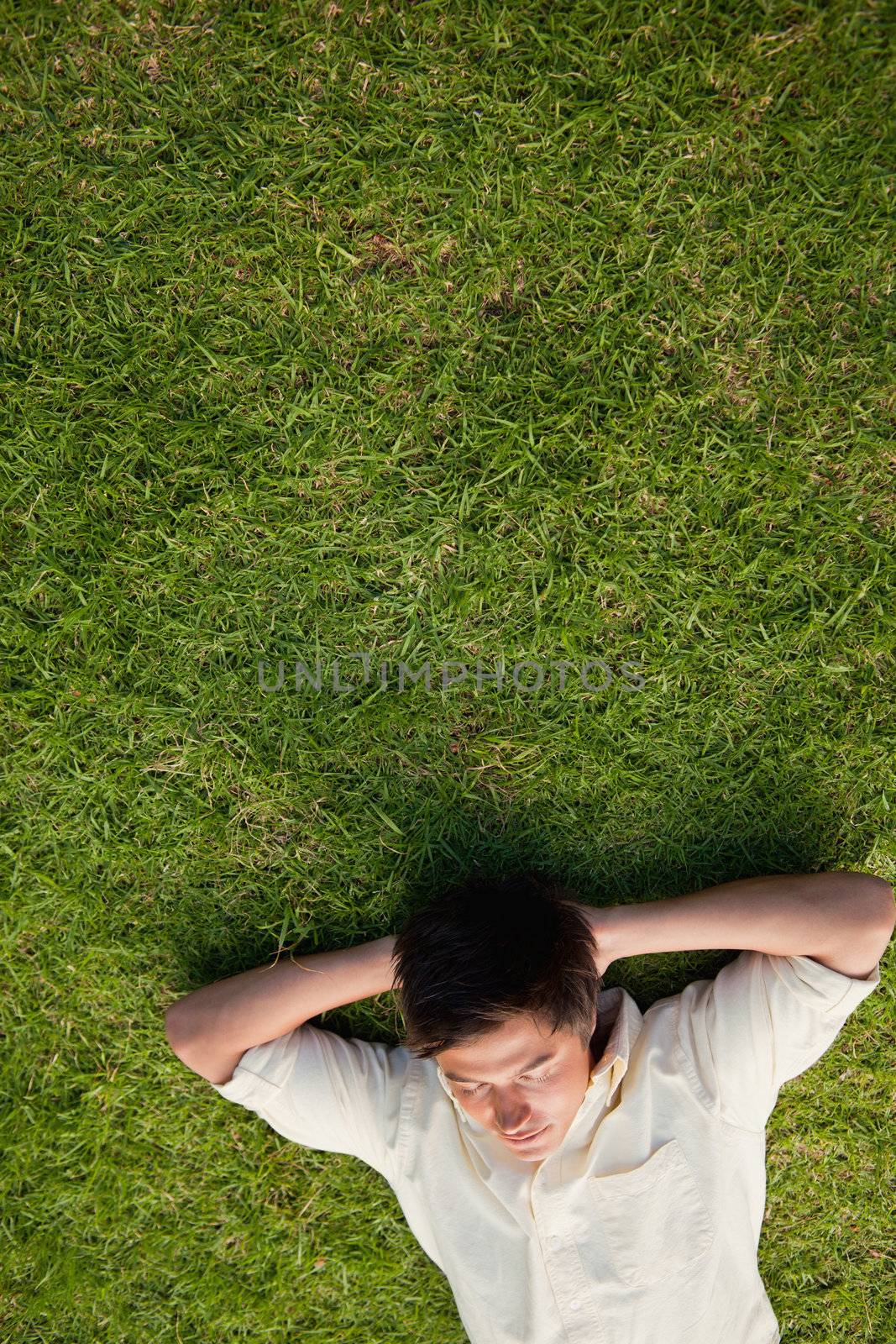 Elevated view of a man lying in grass with his eyes closed and his hands resting underneath his head