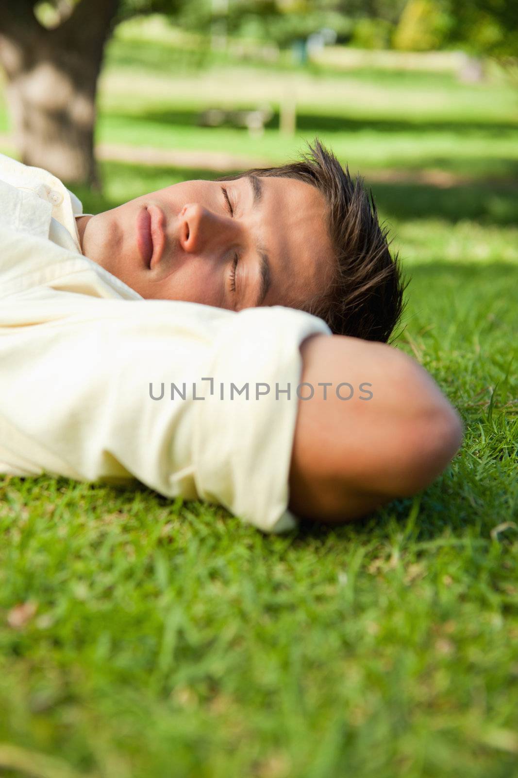 Man lying in grass with his eyes closed and his hands resting underneath the side of his head