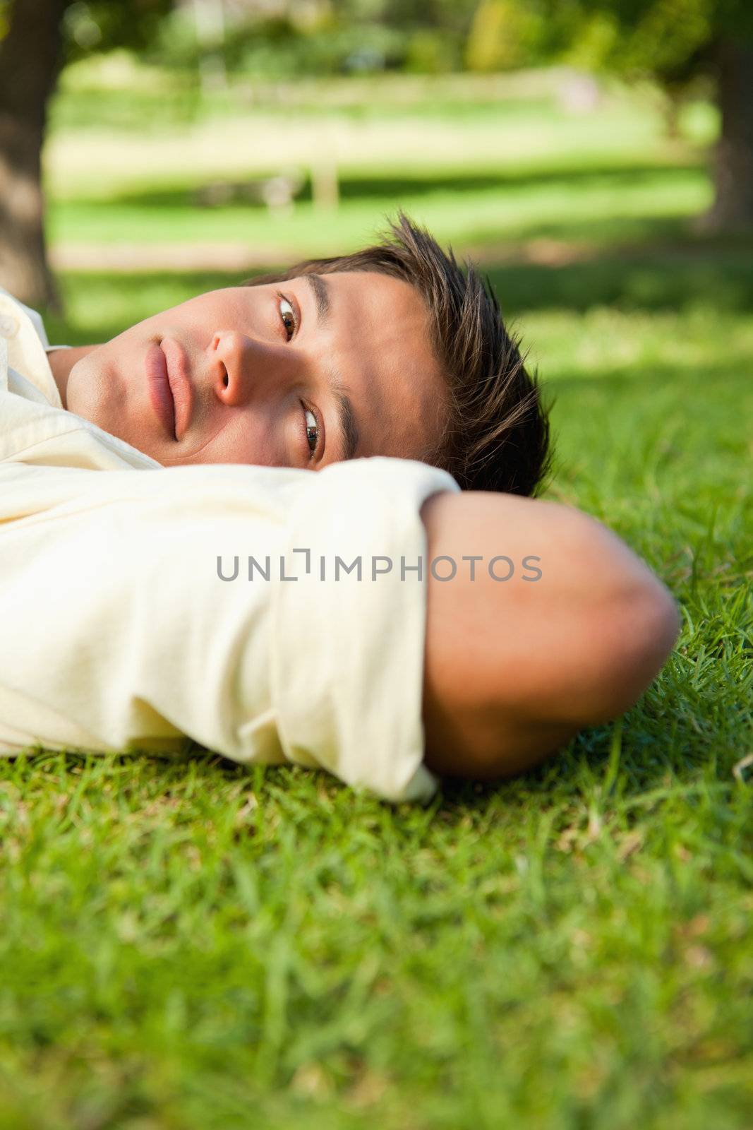Man with serious expression lying in grass with his hands resting underneath the side of his head