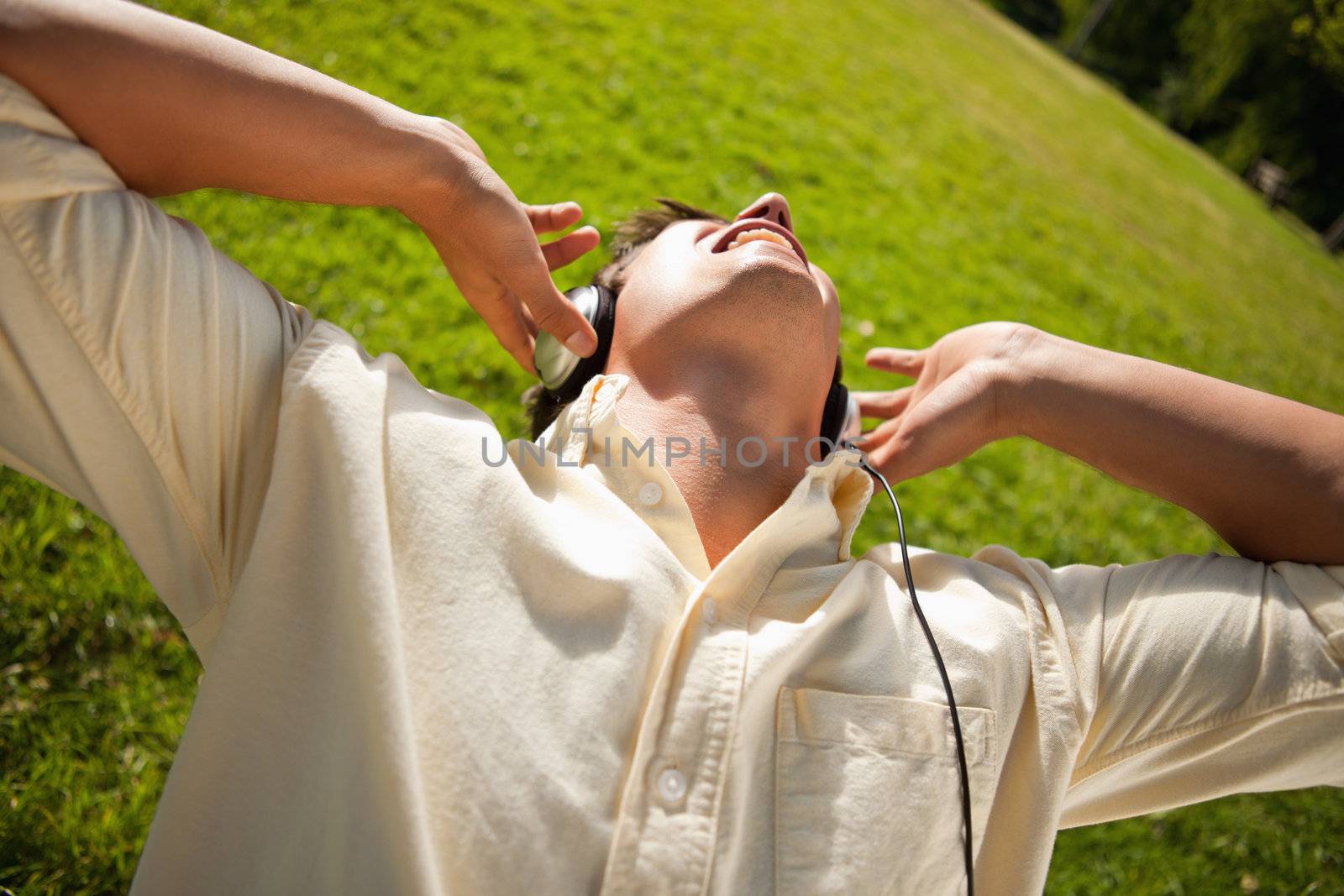 Man singing while using headphones to listen to music as he lies in grass