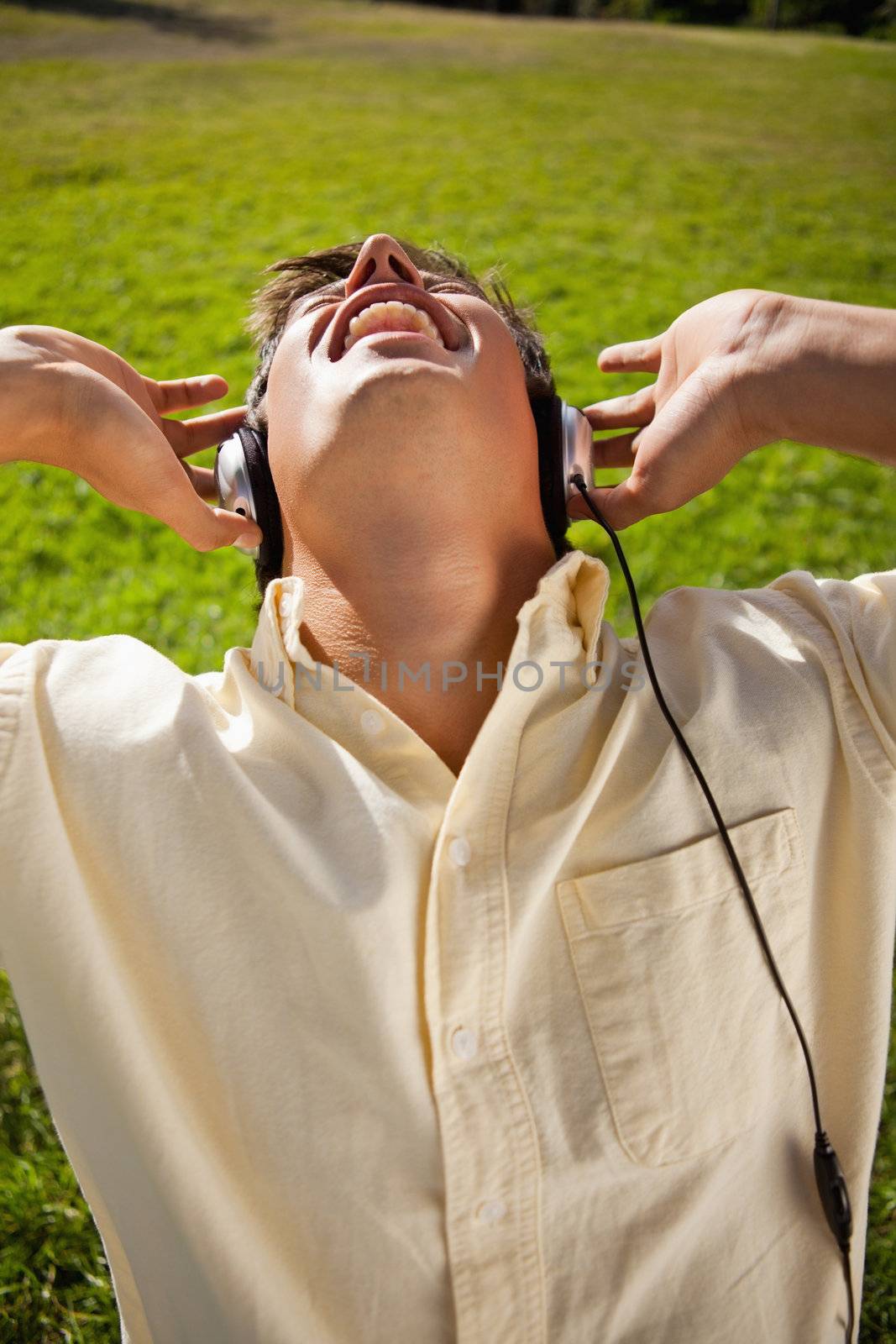 Man singing while using headphones to listen to music as he is sitting in grass