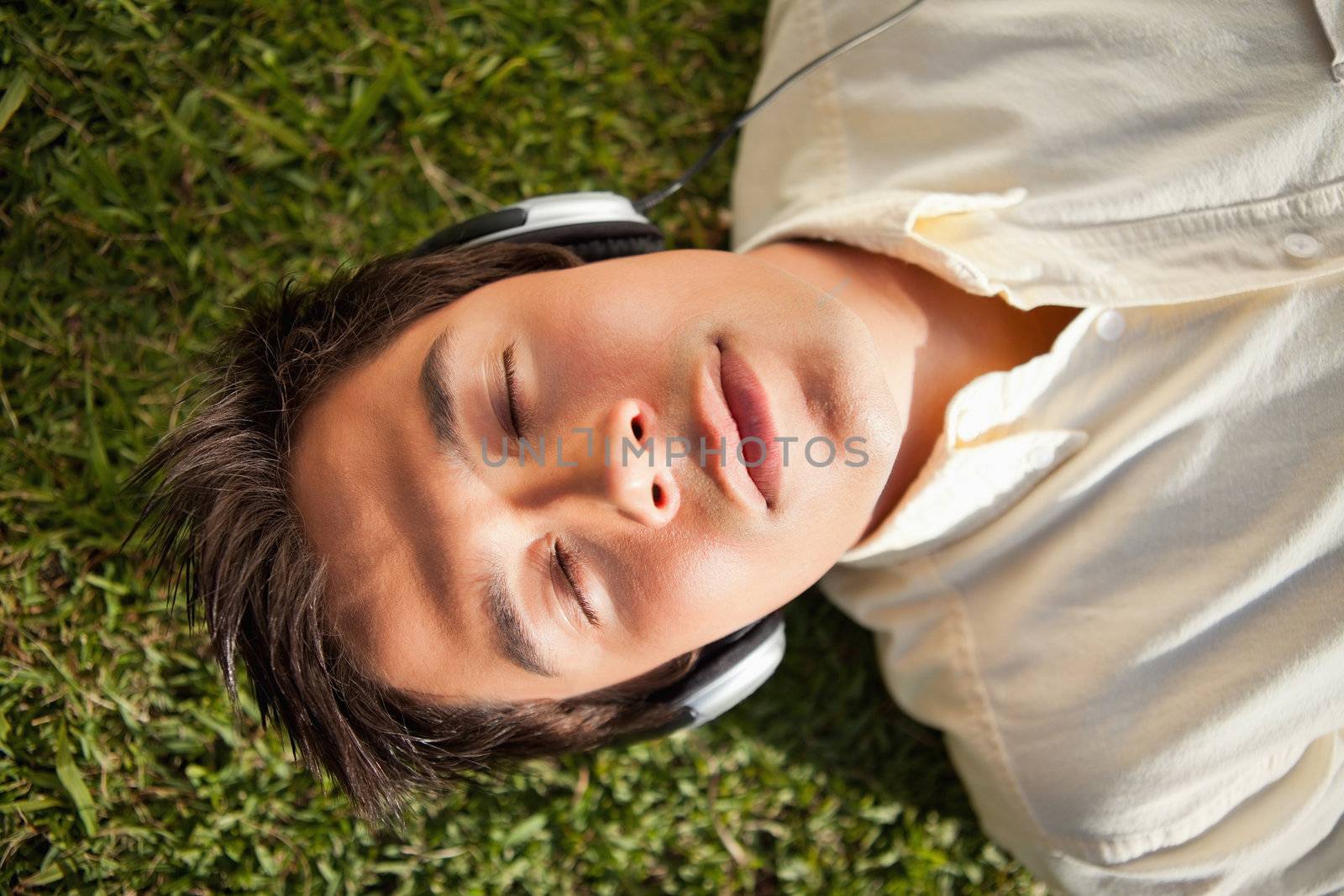 Man with his eyes closed as he uses headphones to listen to music while he lies down on the grass
