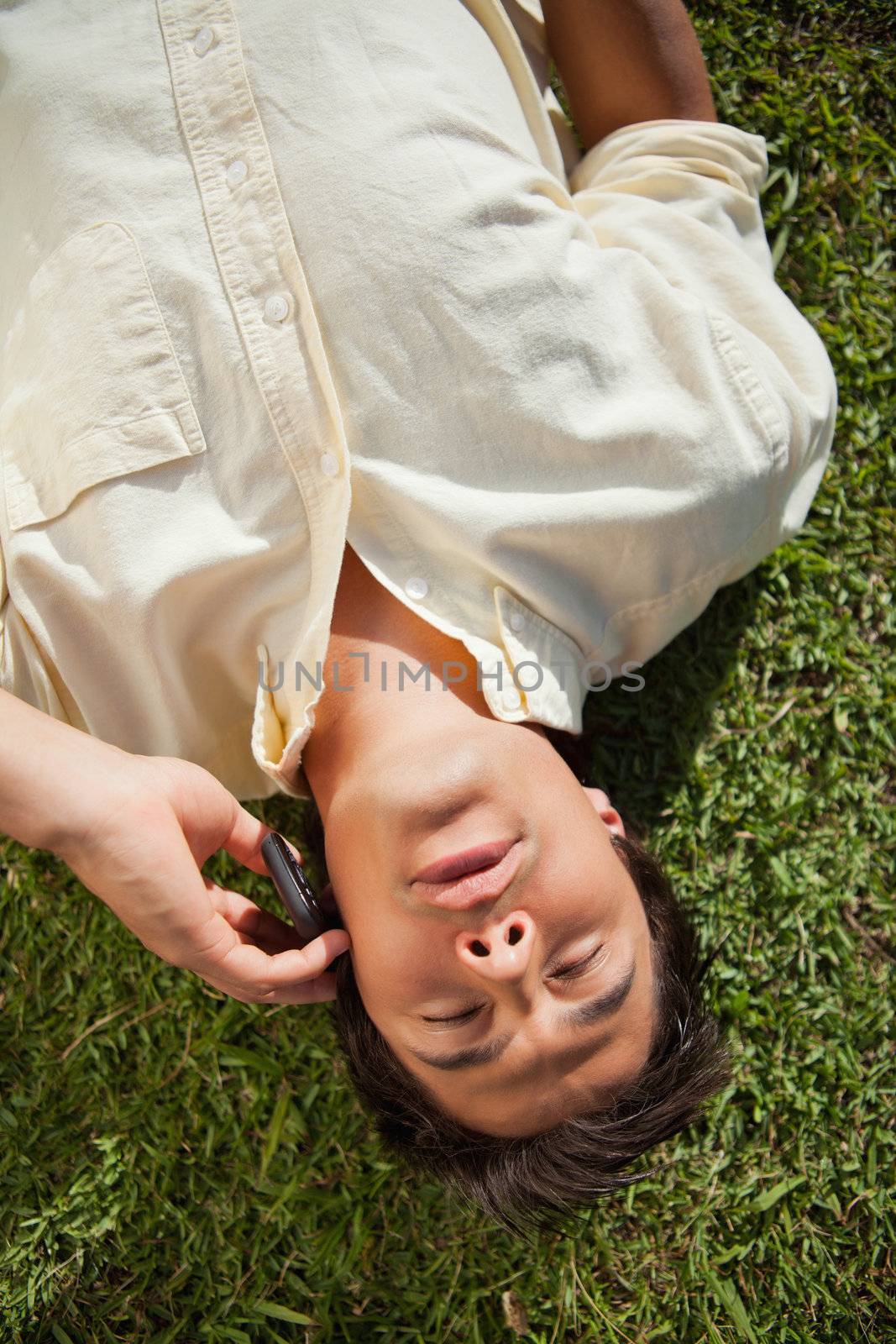 Man with his eyes closed using a mobile phone as he lies down on the grass