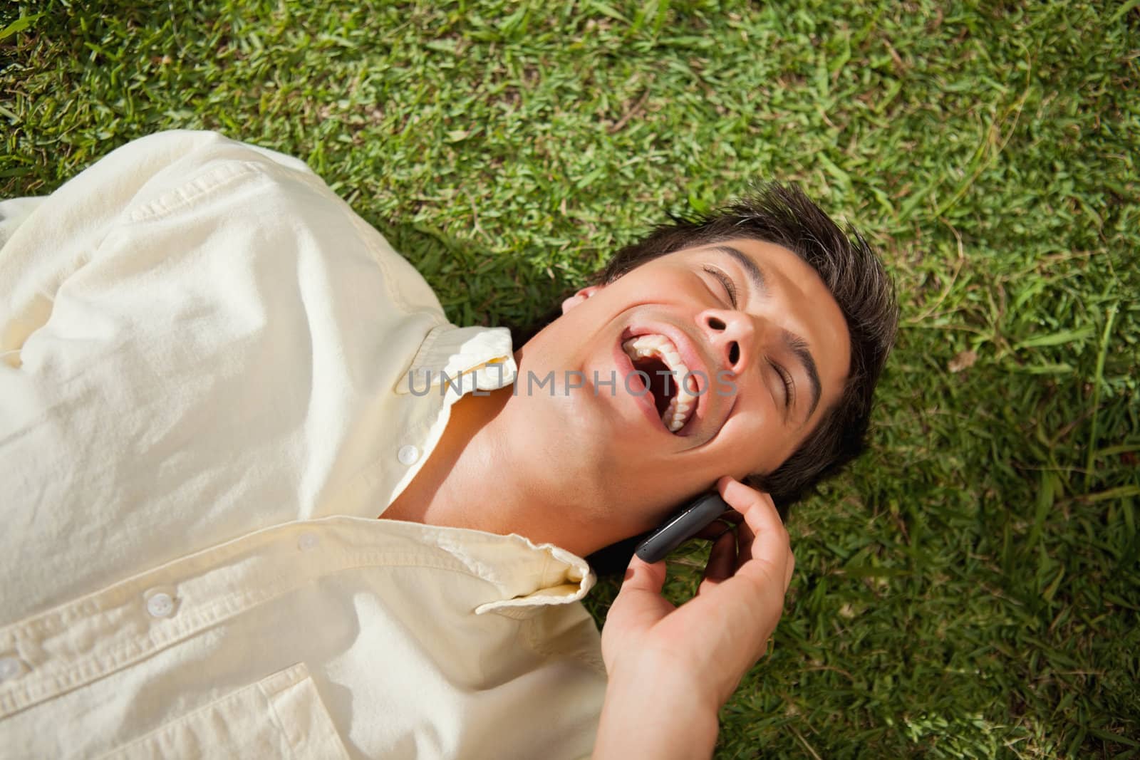 Man laughing while making a call while using a phone as he lies  by Wavebreakmedia